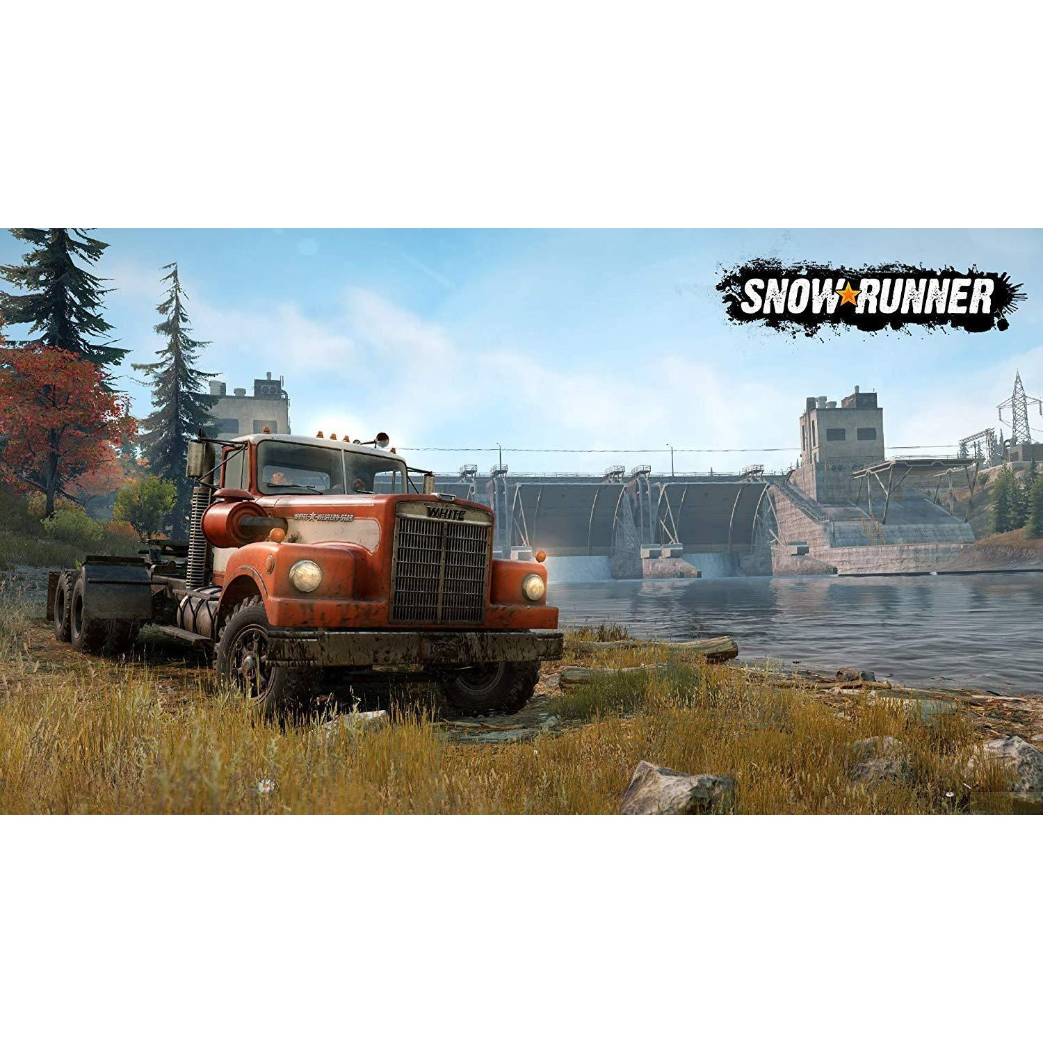 Un camion rouge est assis au bord d'une rivière devant un barrage. Le ciel est bleu.