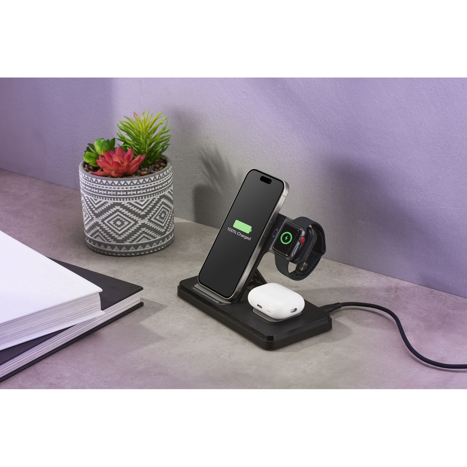 Un supporto di ricarica nero con iPhone, Apple Watch e AirPods su una scrivania.