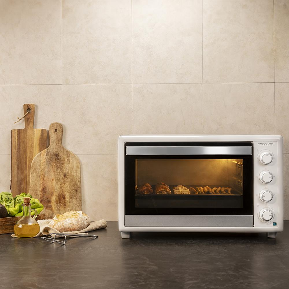 Un mini horno blanco con comida horneada en una encimera con tablas de cortar.