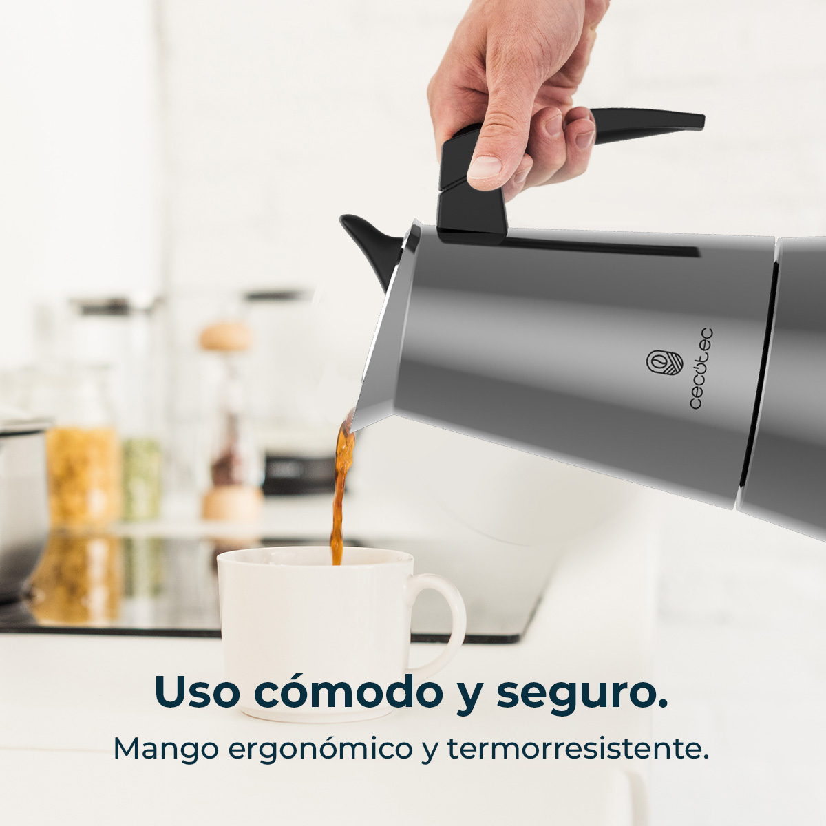 Una mano vierte café de una cafetera gris en una taza blanca.