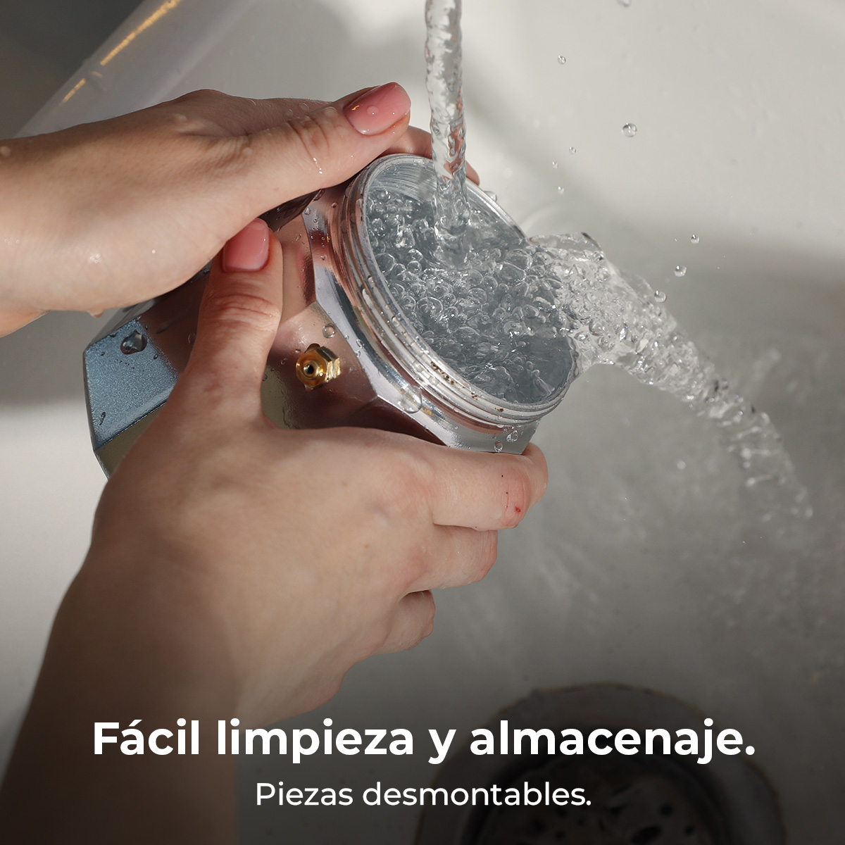 Manos enjuagando una cafetera moka bajo agua corriente en un fregadero.