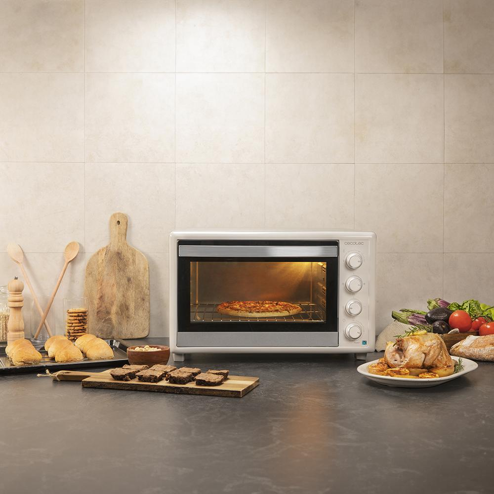 Un horno hornea una pizza, con pollo asado y verduras cerca.