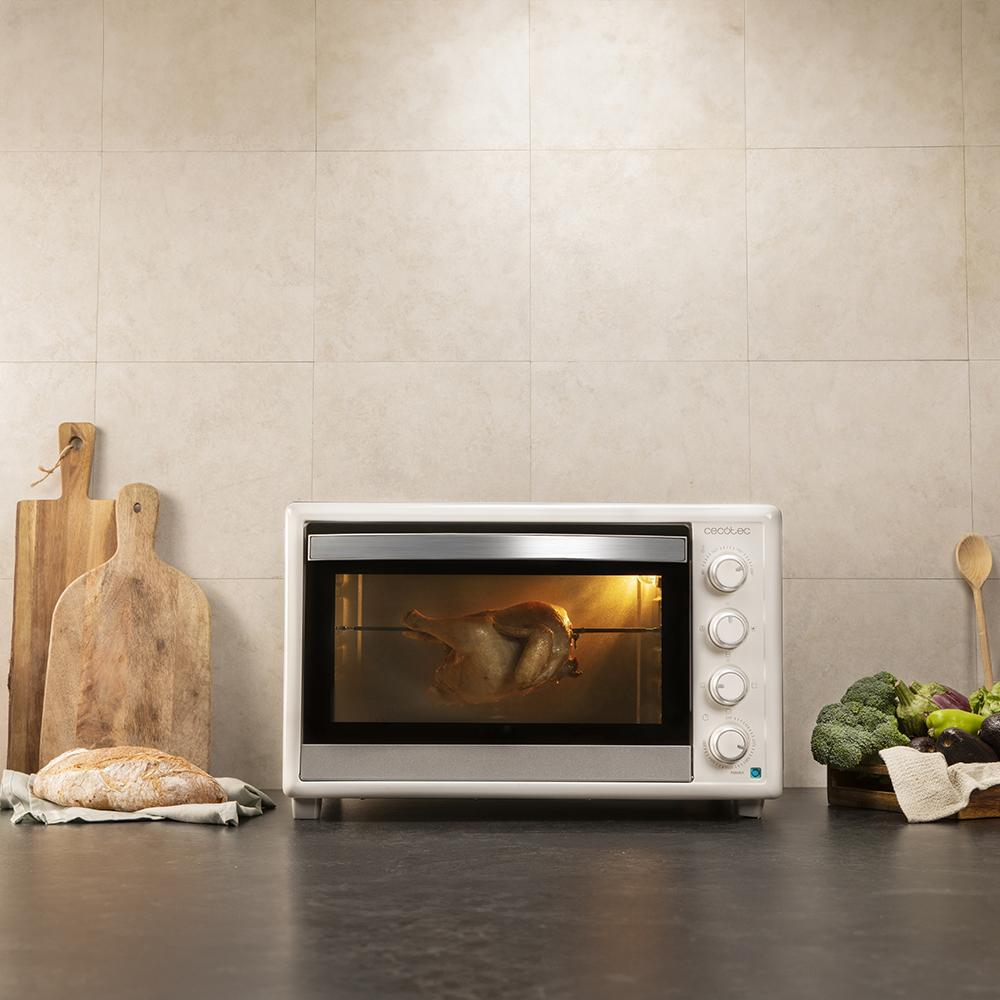 Un pollo entero gira en un horno junto a pan y verduras.