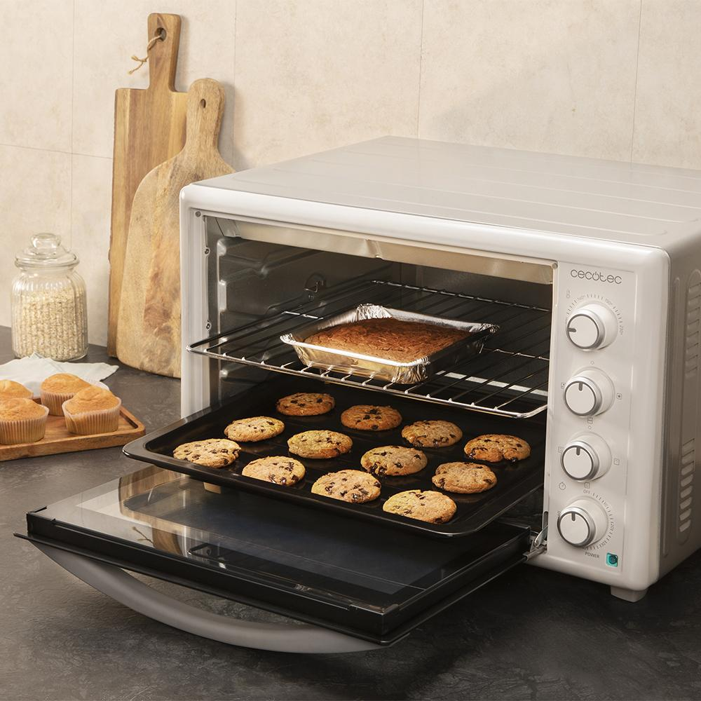 Un horno con galletas y pastel dentro. Varias galletas en una bandeja, pastel en molde de aluminio en la rejilla.