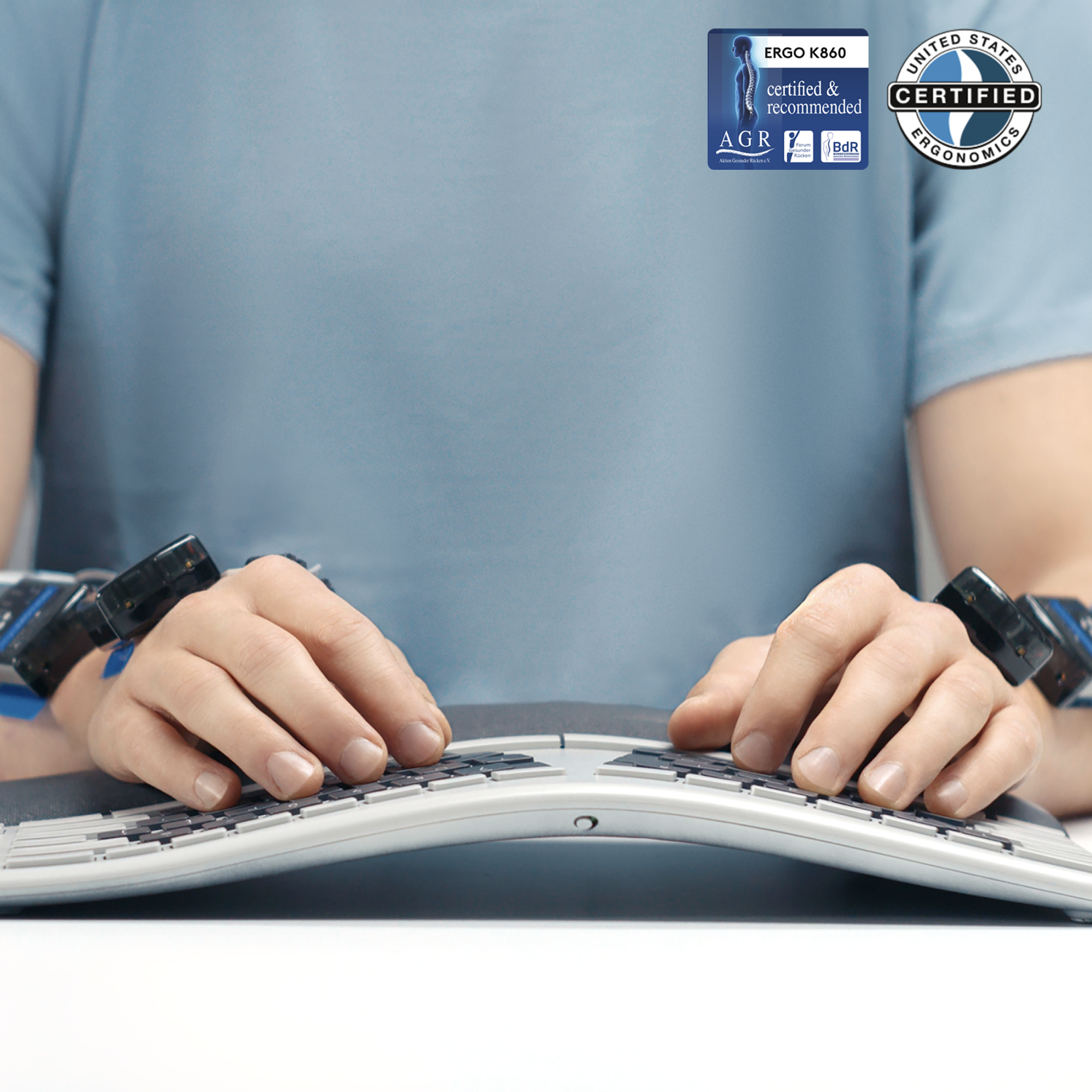 Osoba pisze na klawiaturze ergonomicznej z czujnikami nadgarstka. Loga certyfikacji u góry.