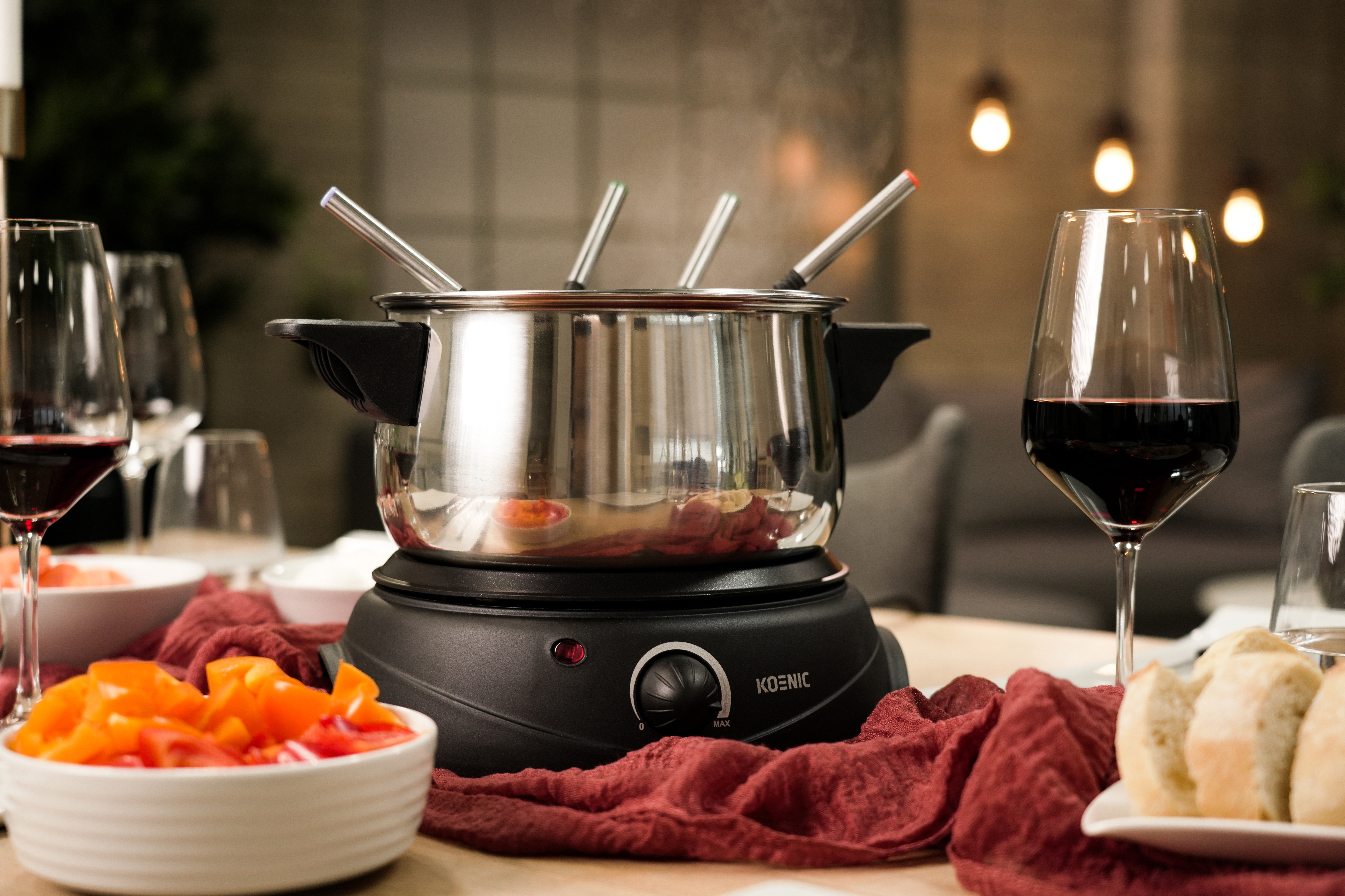 Zestaw do fondue z parującym garnkiem, czerwonym winem i pokrojonymi warzywami.