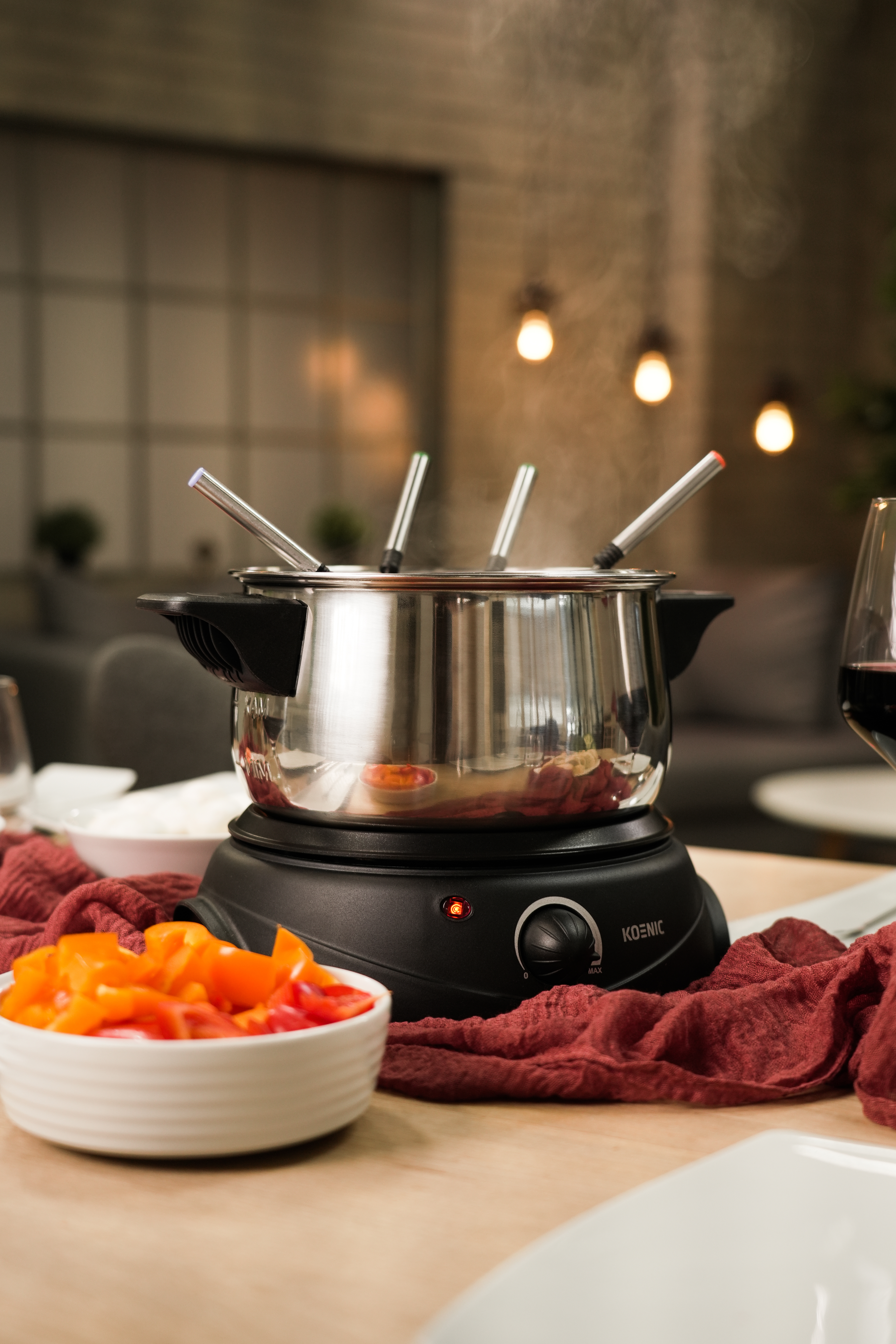 Parująca fontanna fondue na podgrzewanej podstawie, obok miski z posiekaną papryką.