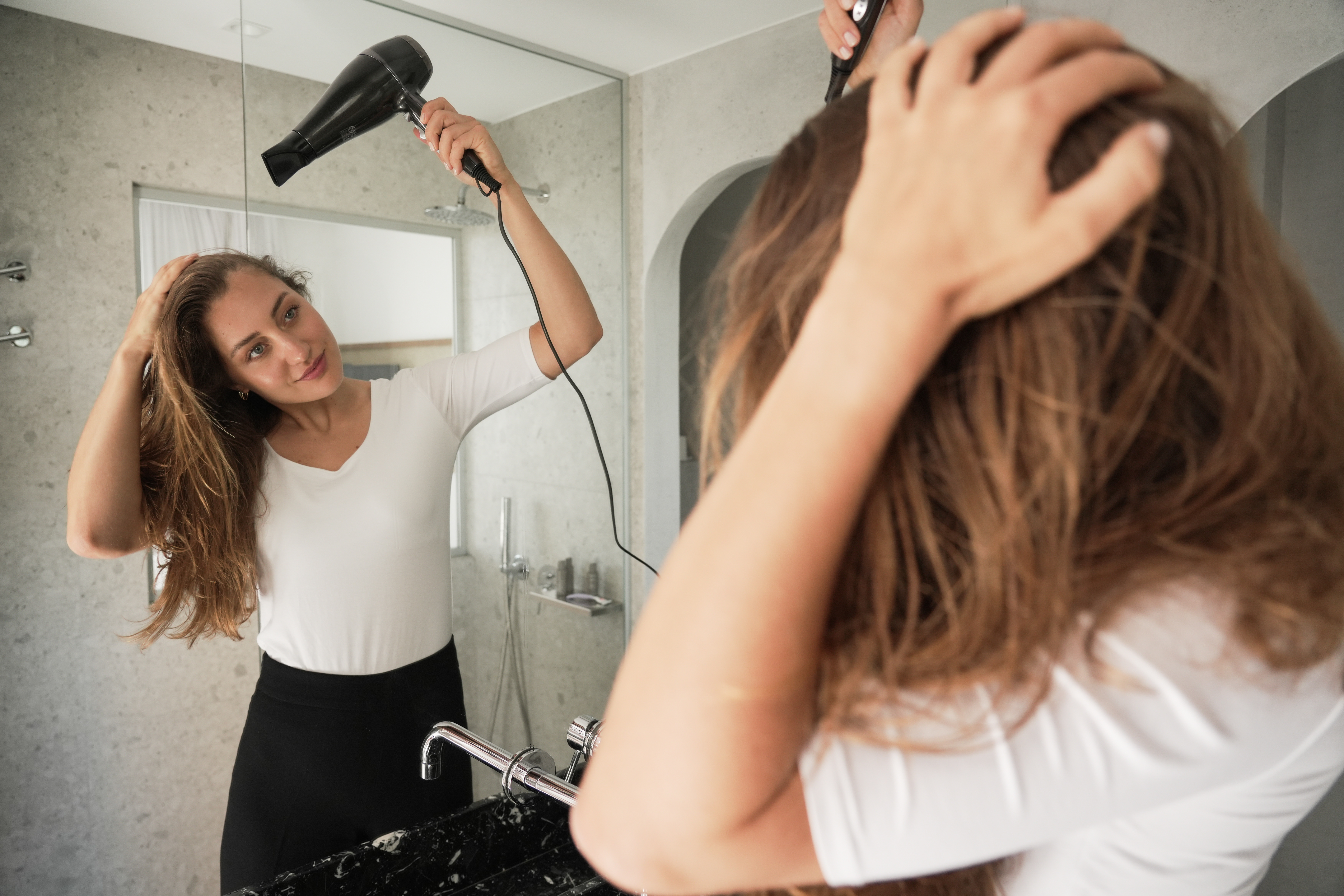 Kobieta suszy długie brązowe włosy czarną suszarką.