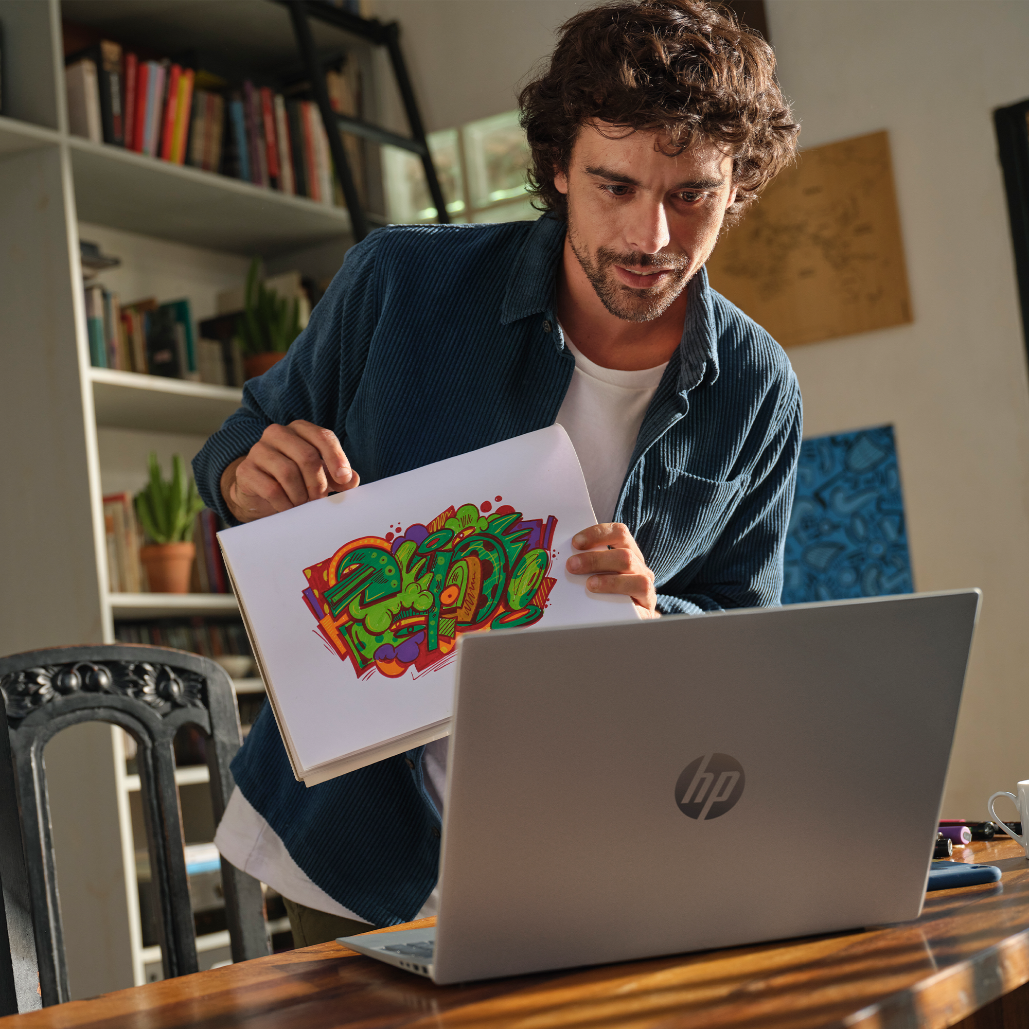 Mężczyzna pokazuje kolorową grafikę graffiti na laptopie, w tle regał z książkami.