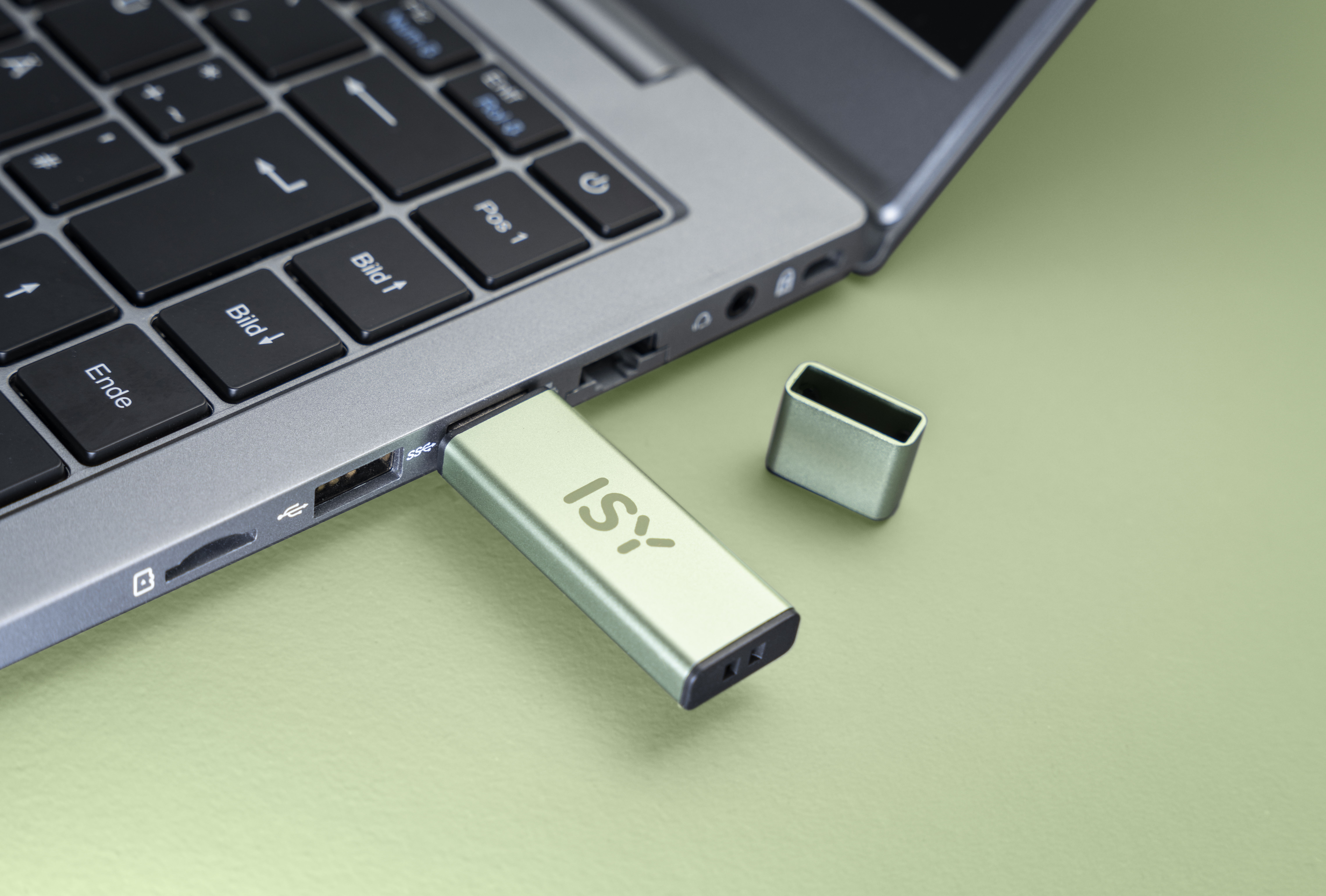 Zielony pendrive jest podłączony do laptopa; obok leży jego nasadka.