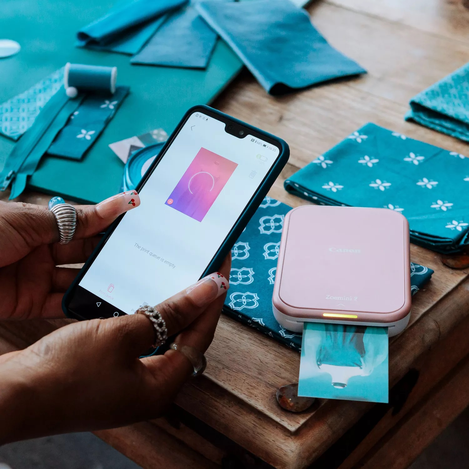 Osoba trzyma smartfon, obok drukarka drukuje zdjęcie.