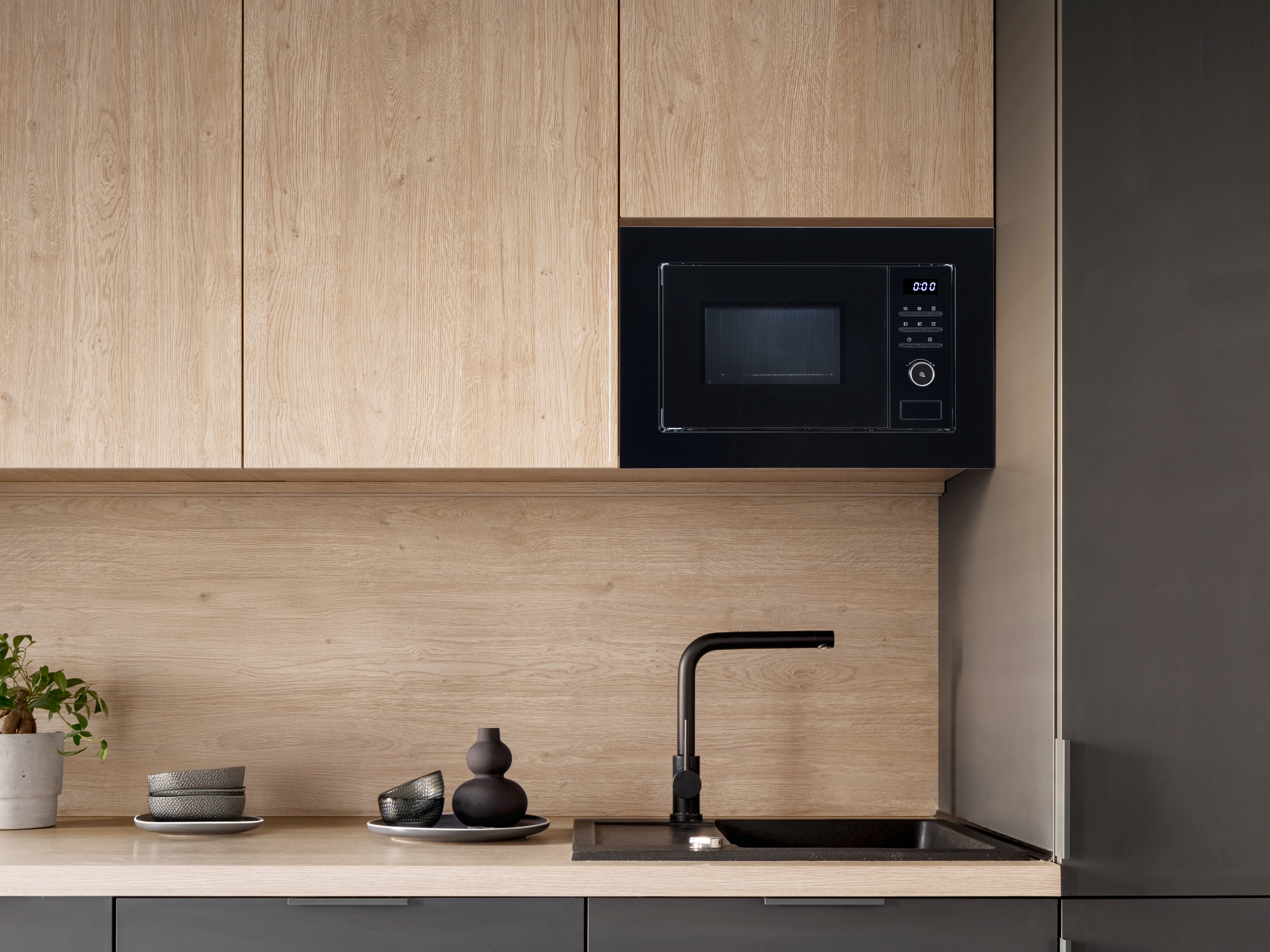 Nowoczesna kuchnia z drewnianymi szafkami, czarnym mikrofalowym i zlewem.
