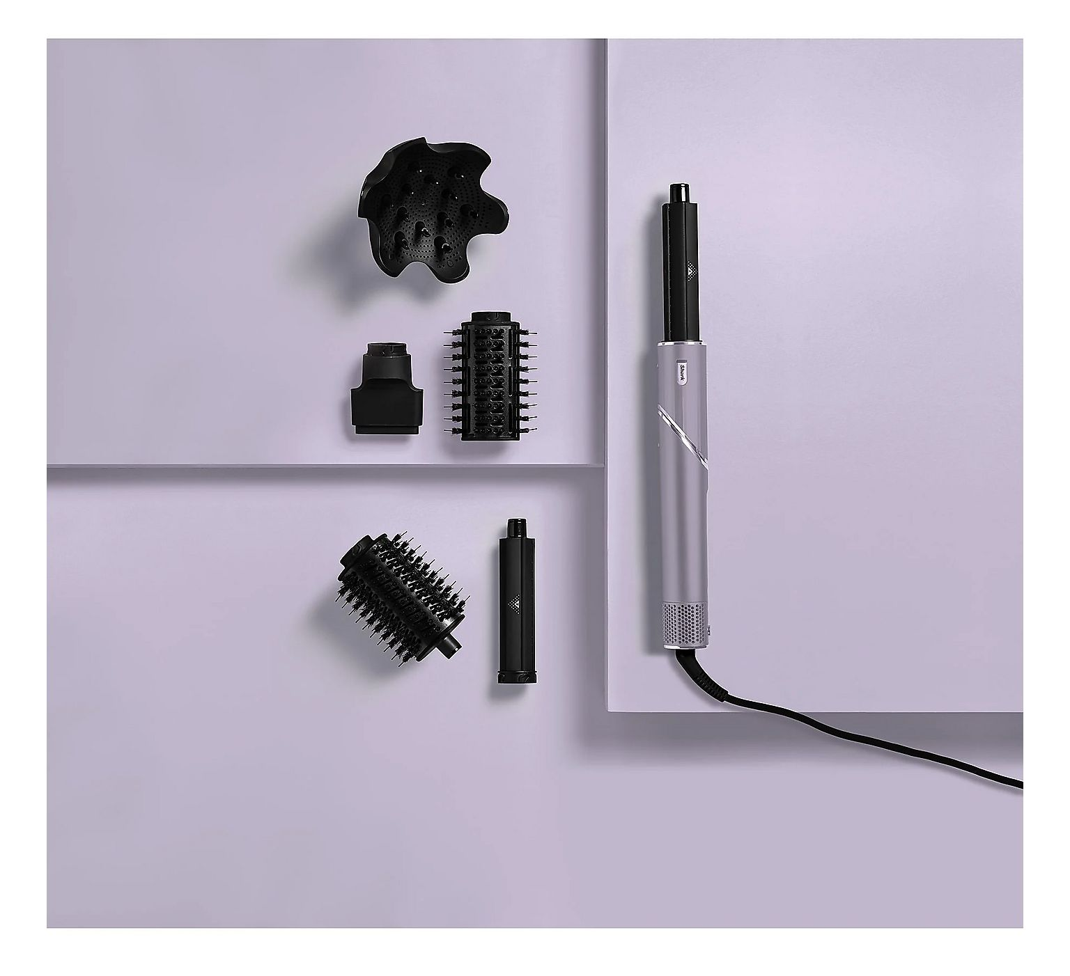 Un coiffeur argenté avec accessoires noirs, brosses et diffuseur, sur surface violet clair.