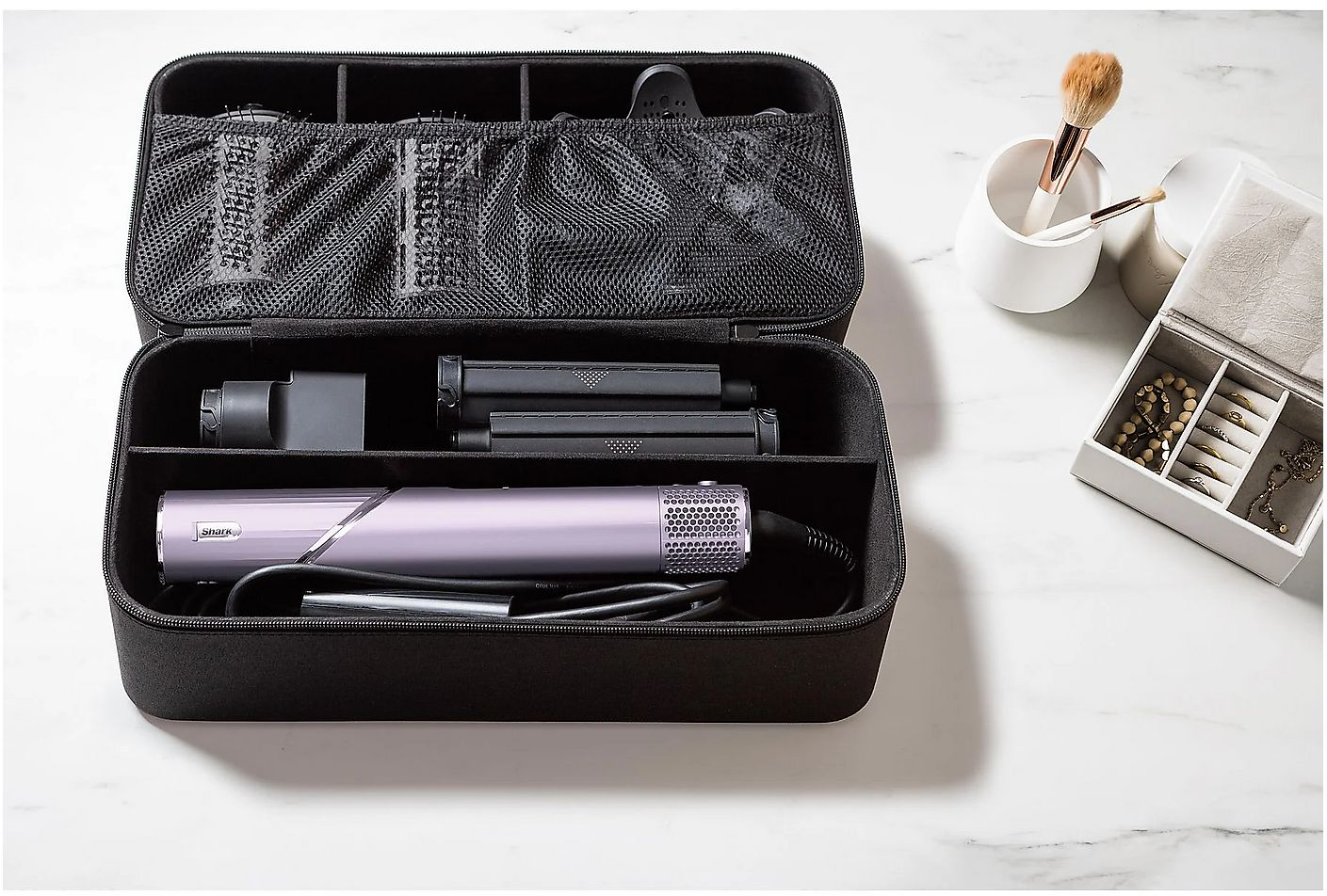 Une trousse noire ouverte avec des outils capillaires et accessoires sur marbre.