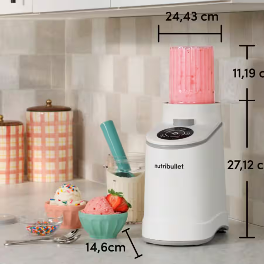 Un mixeur Nutribullet blanc avec un smoothie rose dans la tasse, de la glace et des vermicelles.
