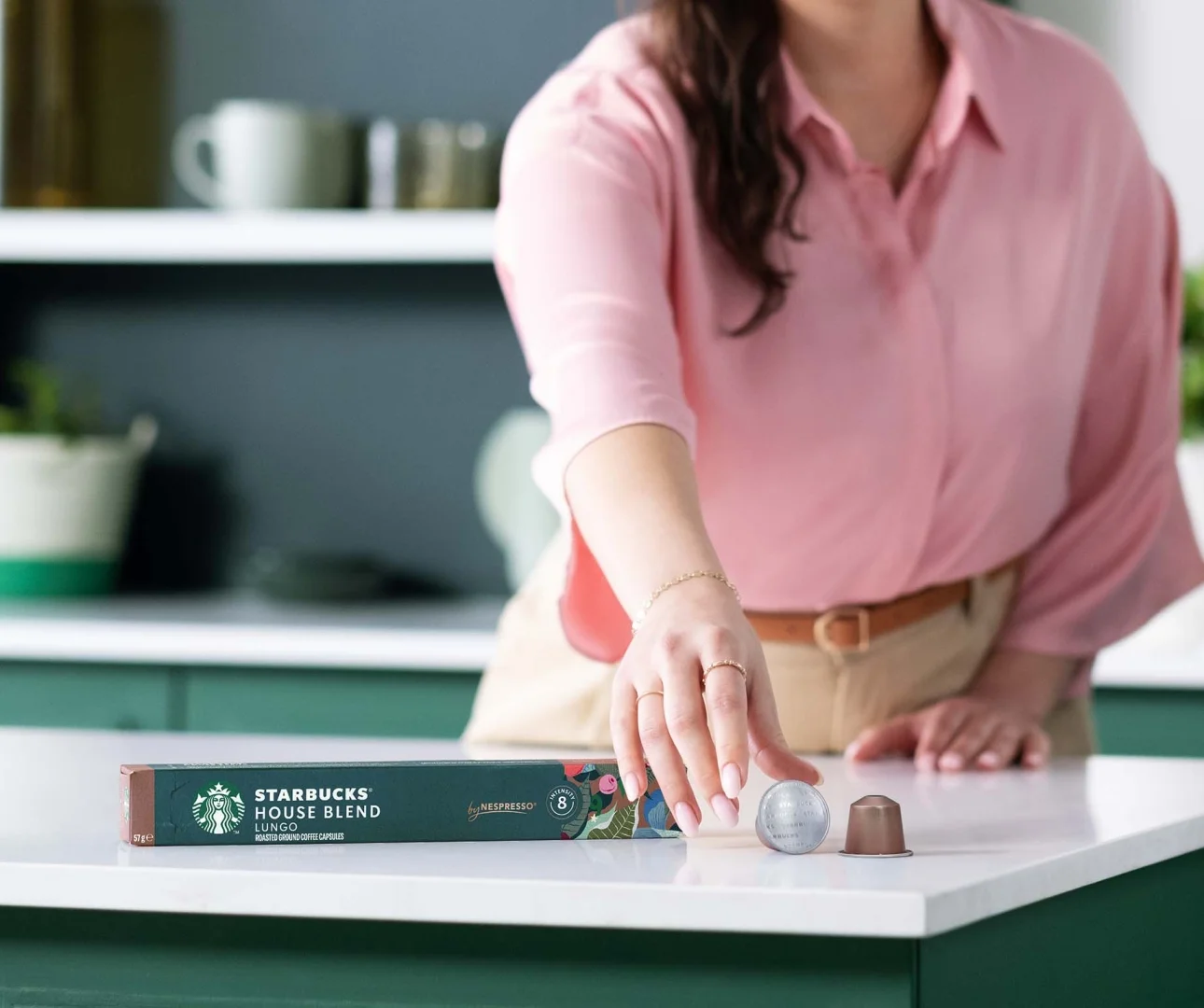 Femme en chemisier rose choisit une capsule de café près d'une boîte Starbucks.