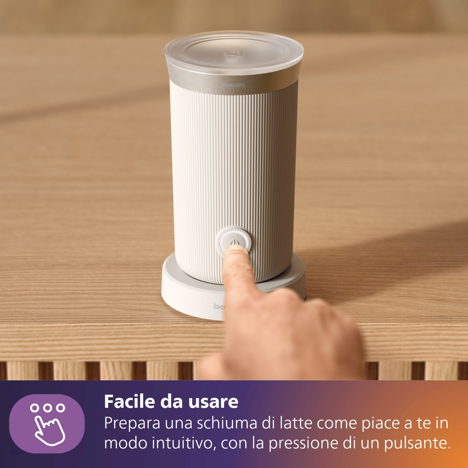 Un dito preme il pulsante di un montalatte Philips bianco su un tavolo di legno.
