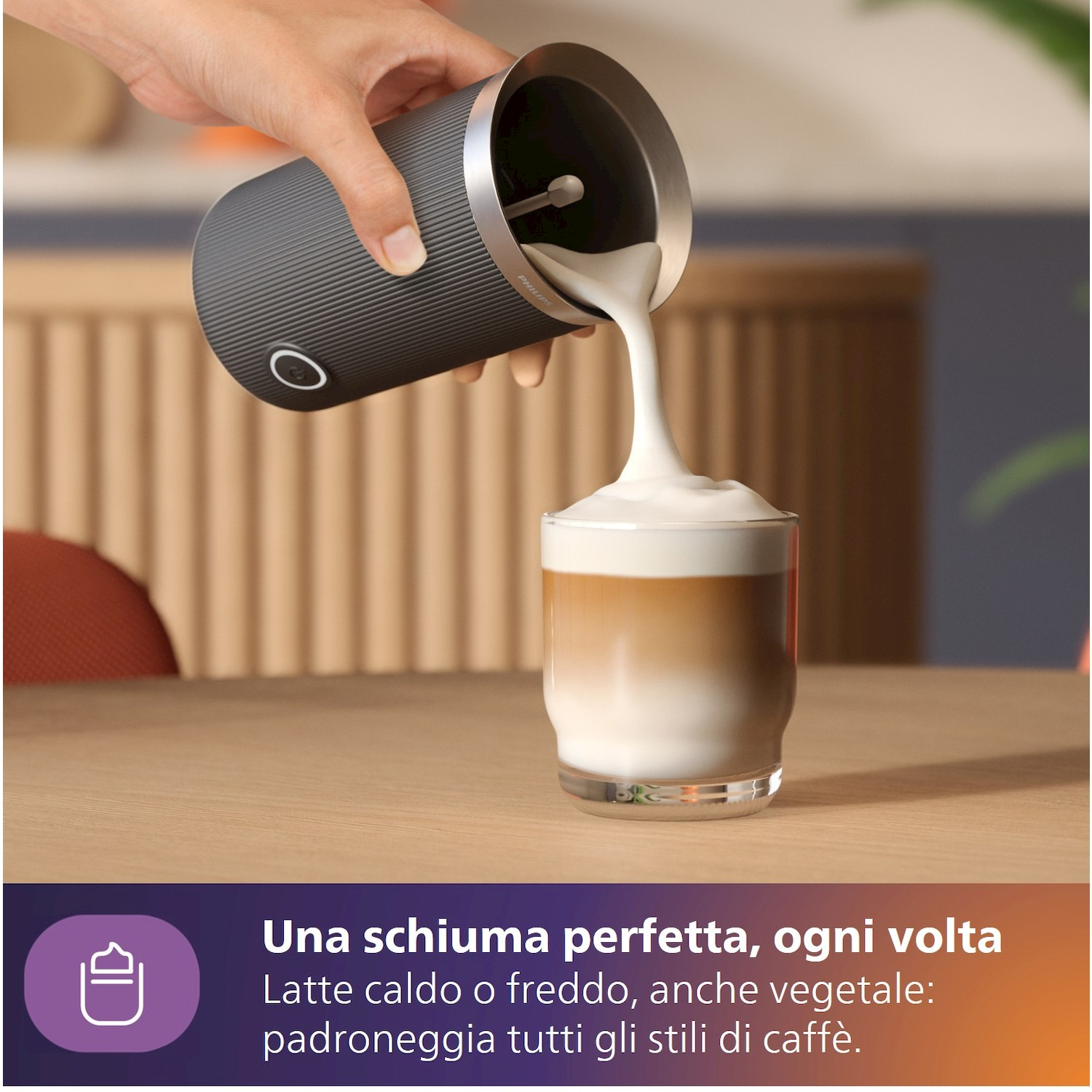 Una mano versa schiuma di latte cremosa da un dispositivo scuro in un bicchiere di latte.
