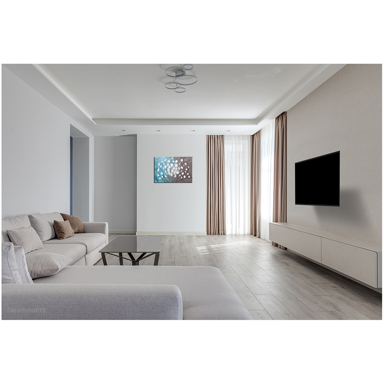 Een lichte woonkamer met bank, salontafel, tv en schilderij.