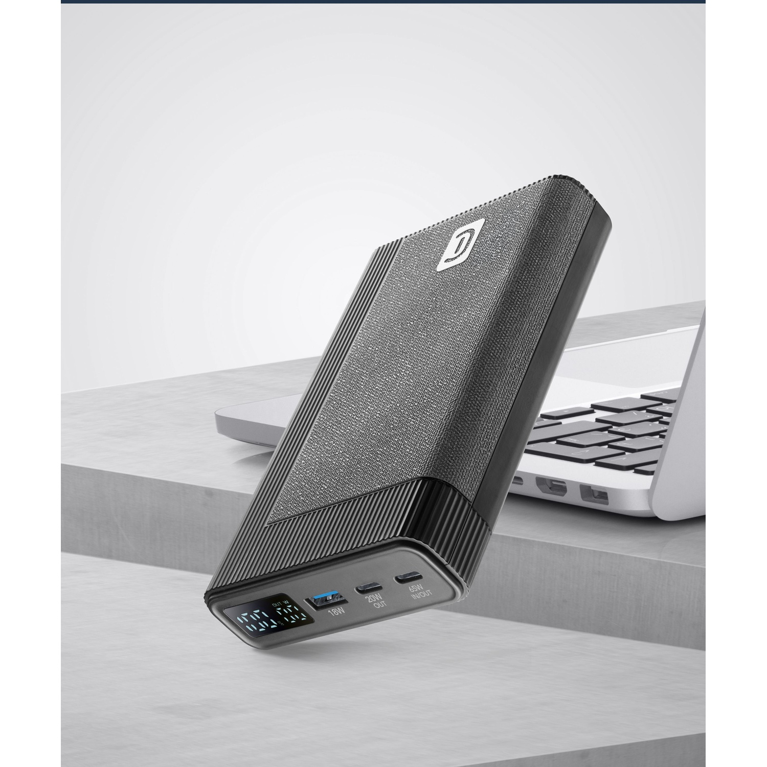 Power bank nero con display digitale accanto a un laptop su una superficie grigia.