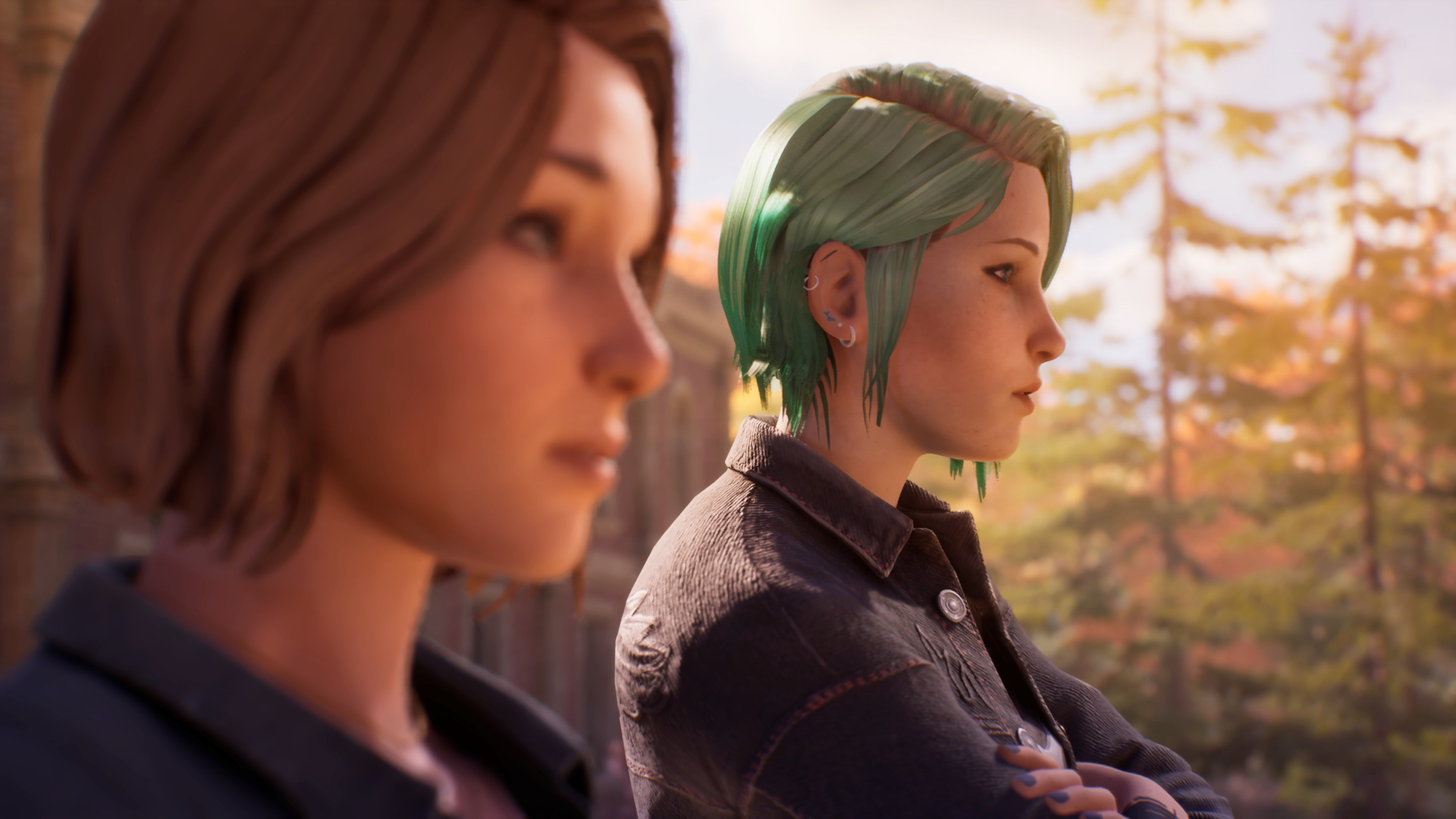 Deux jeunes femmes, l'une aux cheveux bruns, l'autre verts, regardent à droite. Arrière-plan flou.