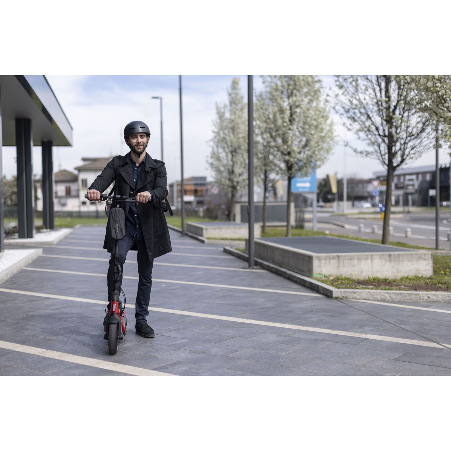 Un uomo con casco guida un monopattino elettrico rosso su un marciapiede.