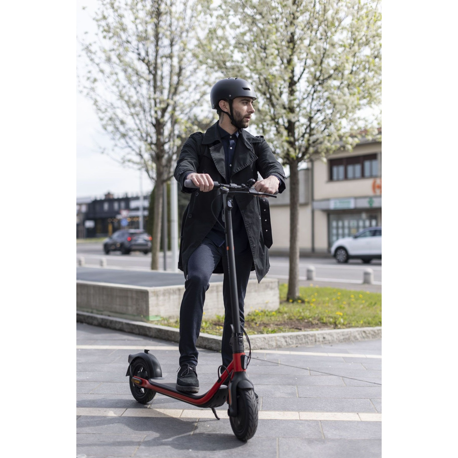 Un uomo con casco è in piedi su un monopattino elettrico rosso su un marciapiede.