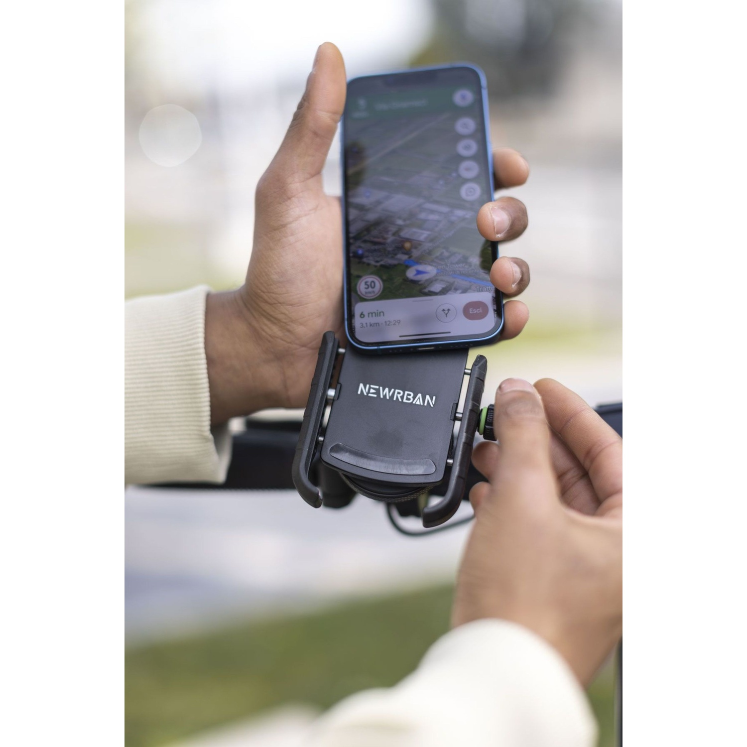 Una mano tiene uno smartphone con app di navigazione, montato su un supporto.