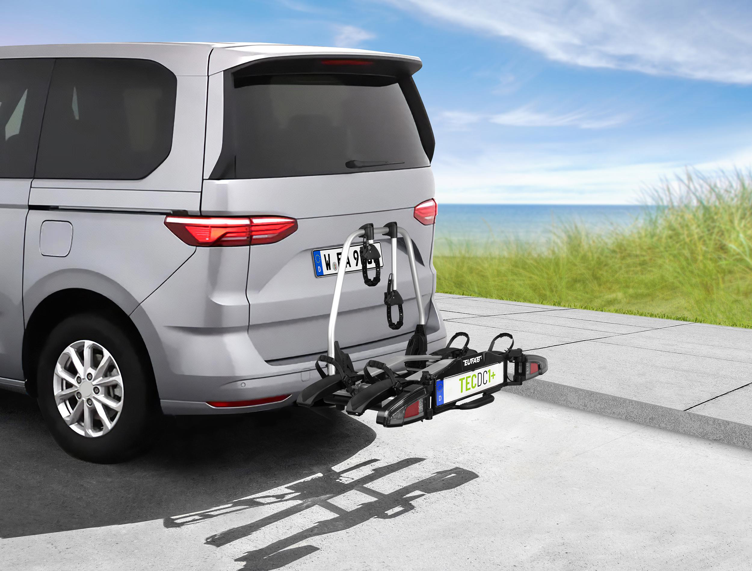 Silberner Van mit Fahrradträger am Heck, am Meer.
