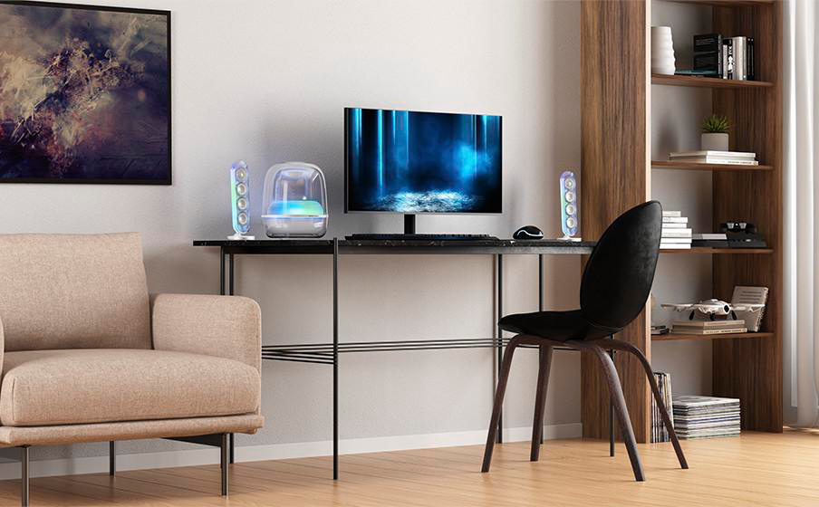 Ein Schreibtisch mit Monitor, Tastatur, Maus und Lautsprechern, daneben ein Sessel und ein Bücherregal.