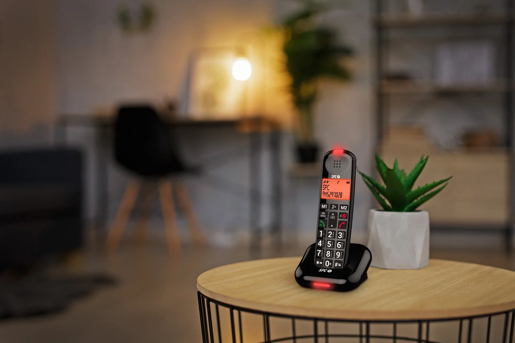 Un teléfono inalámbrico negro con luz de carga roja está sobre una mesa de madera.