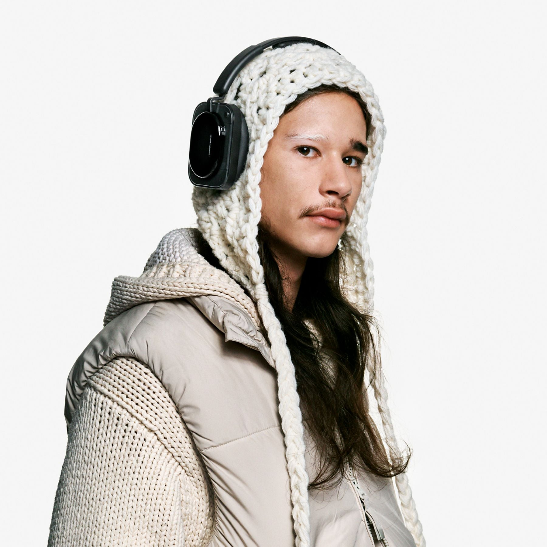 Una persona con auriculares y capucha de ganchillo, con una chaqueta acolchada beige.