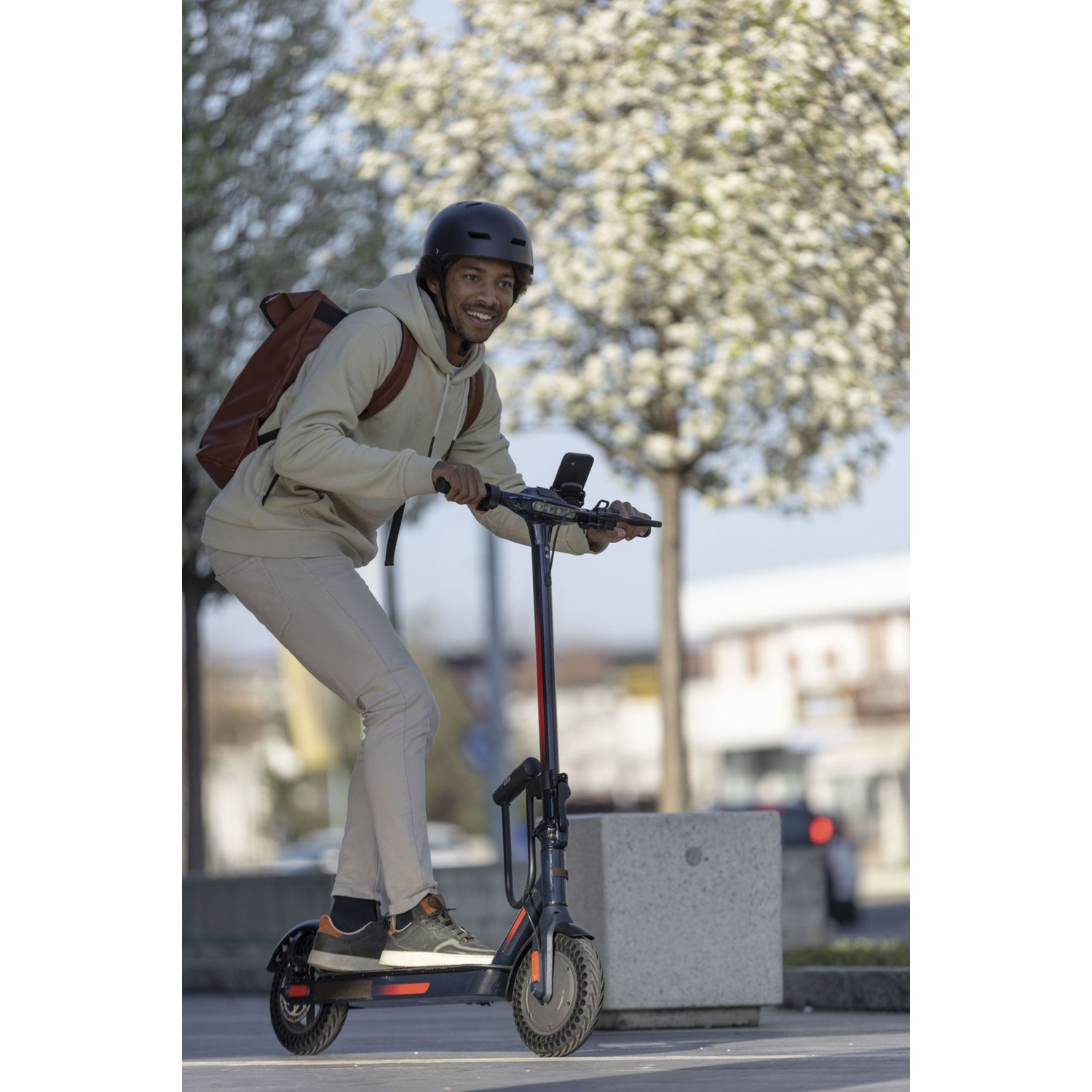Un uomo con casco guida un monopattino elettrico con zaino.