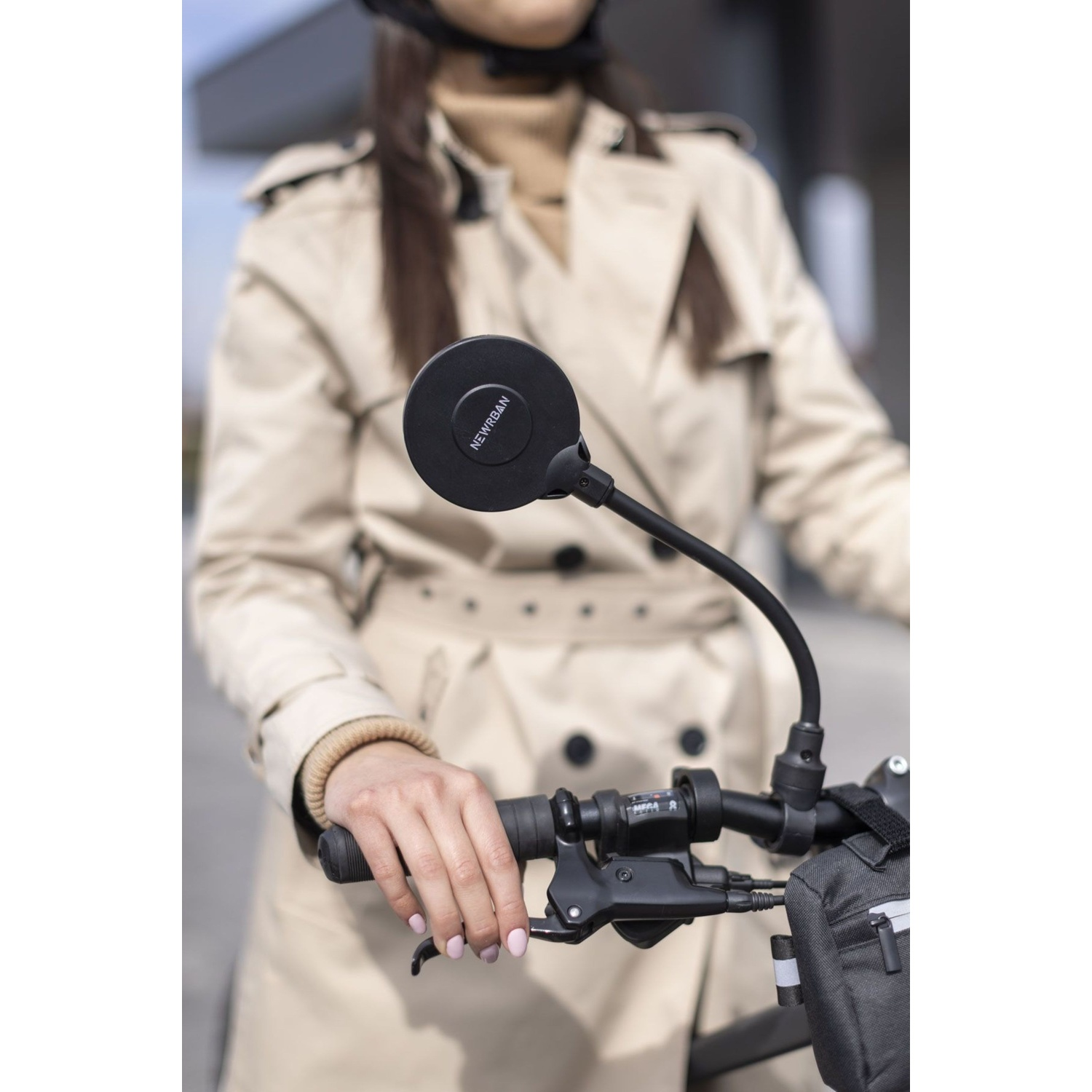 Donna in trench beige e casco tiene manubrio bici.