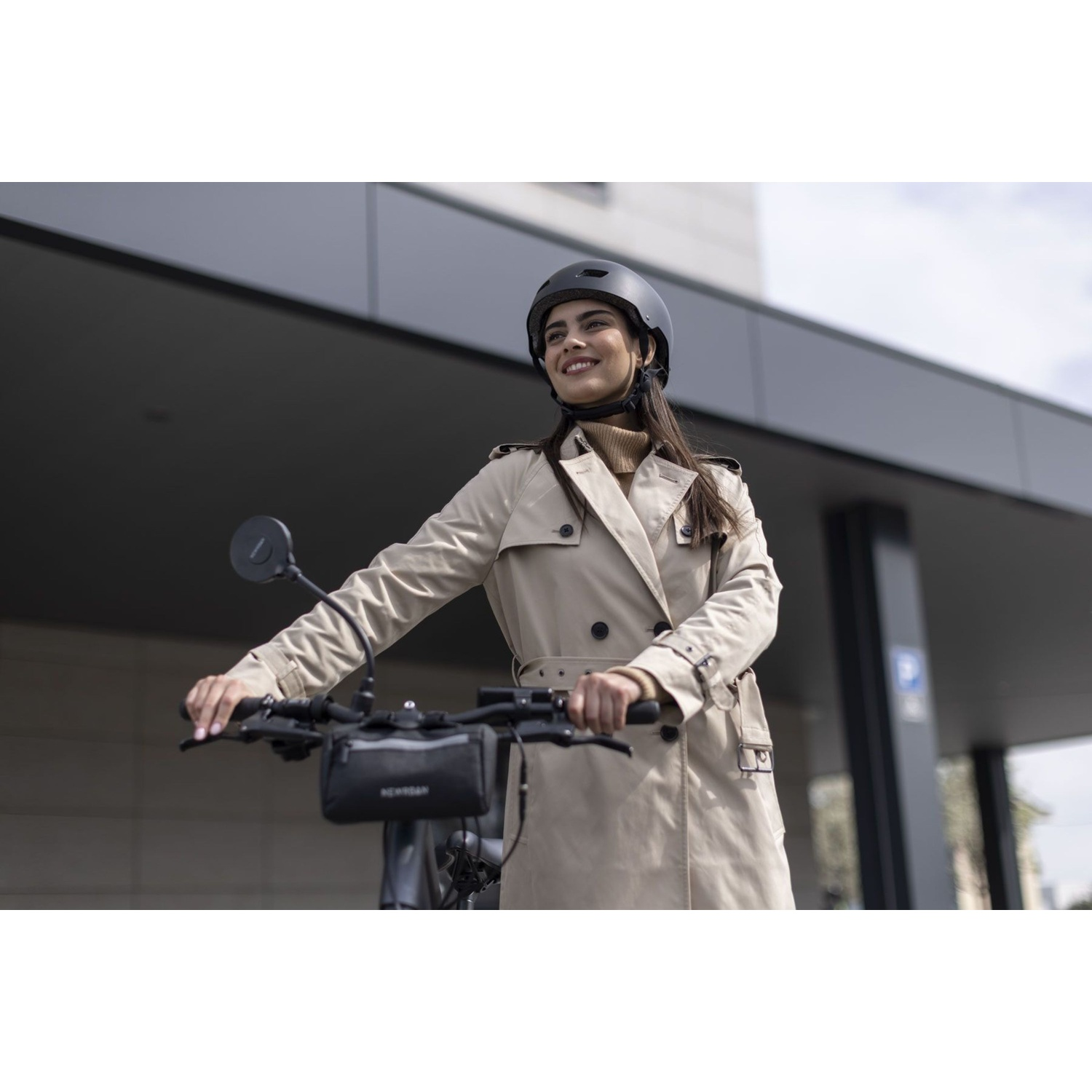 Donna con casco e trench beige su scooter davanti a edificio moderno.