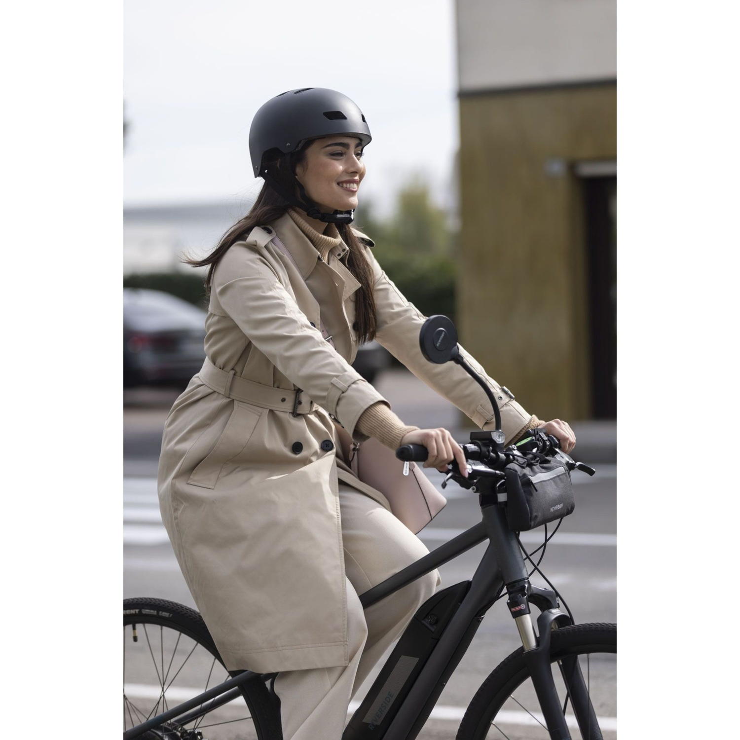 Donna in trench beige e casco va in bicicletta, sorridendo.