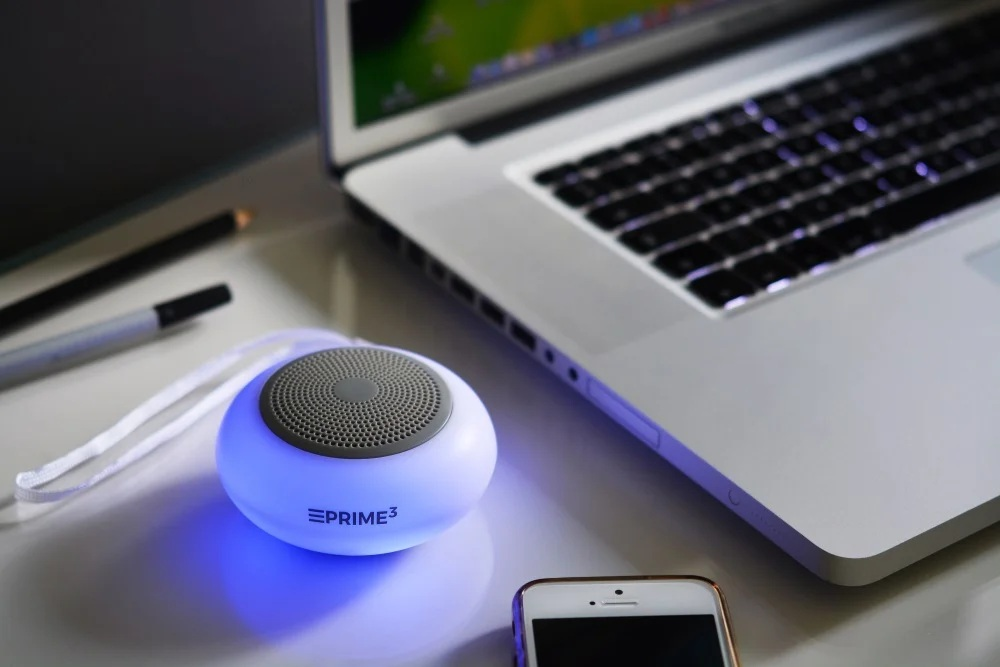 Świecący niebieski głośnik obok laptopa i smartfona.