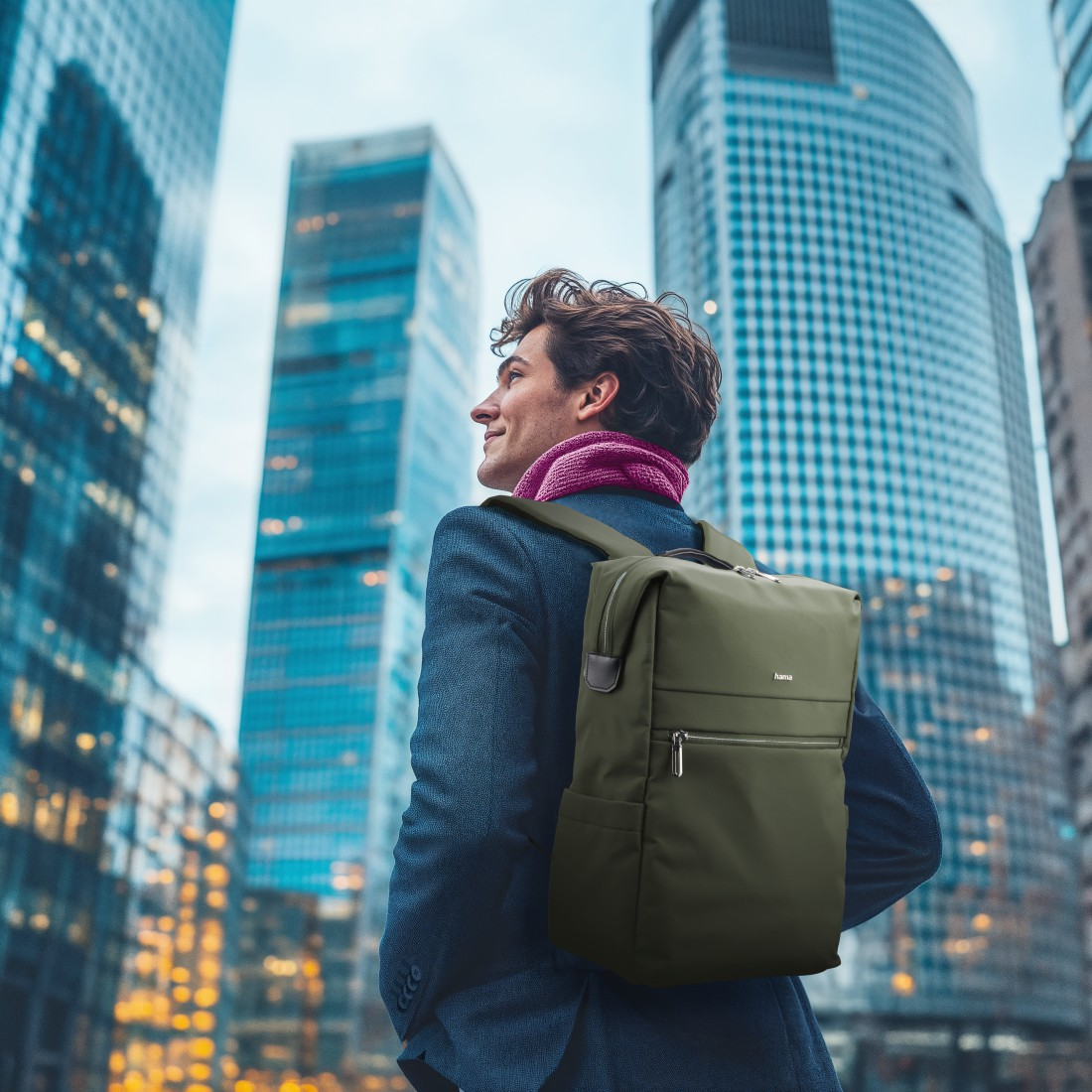 Mann mit grünem Rucksack vor Wolkenkratzern in der Stadt.