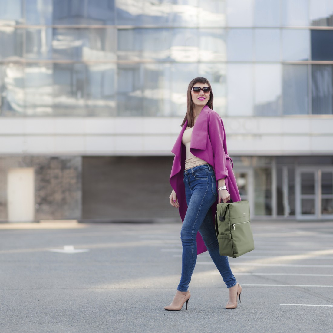 Frau in Pink, Jeans und hohen Schuhen geht mit Rucksack.