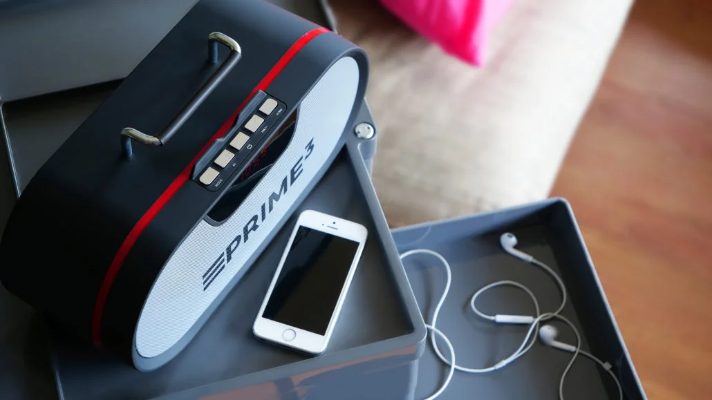 Czarny głośnik z czerwoną linią, biały smartfon i słuchawki na tacy.