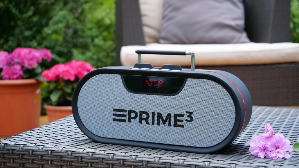 Czarny głośnik z czerwonym wykończeniem stoi na stole. Kwiaty w tle.