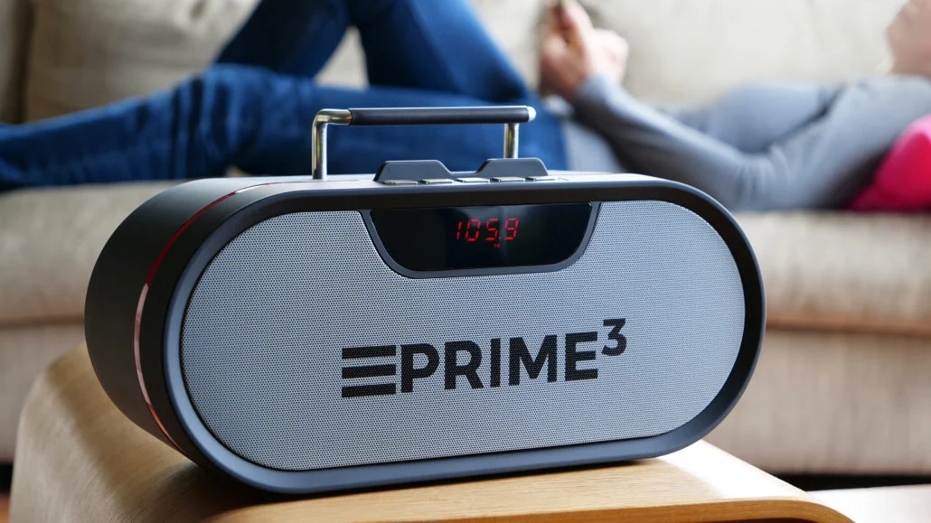 Przenośny głośnik z czerwonym wyświetlaczem stoi na stole. W tle leży osoba.