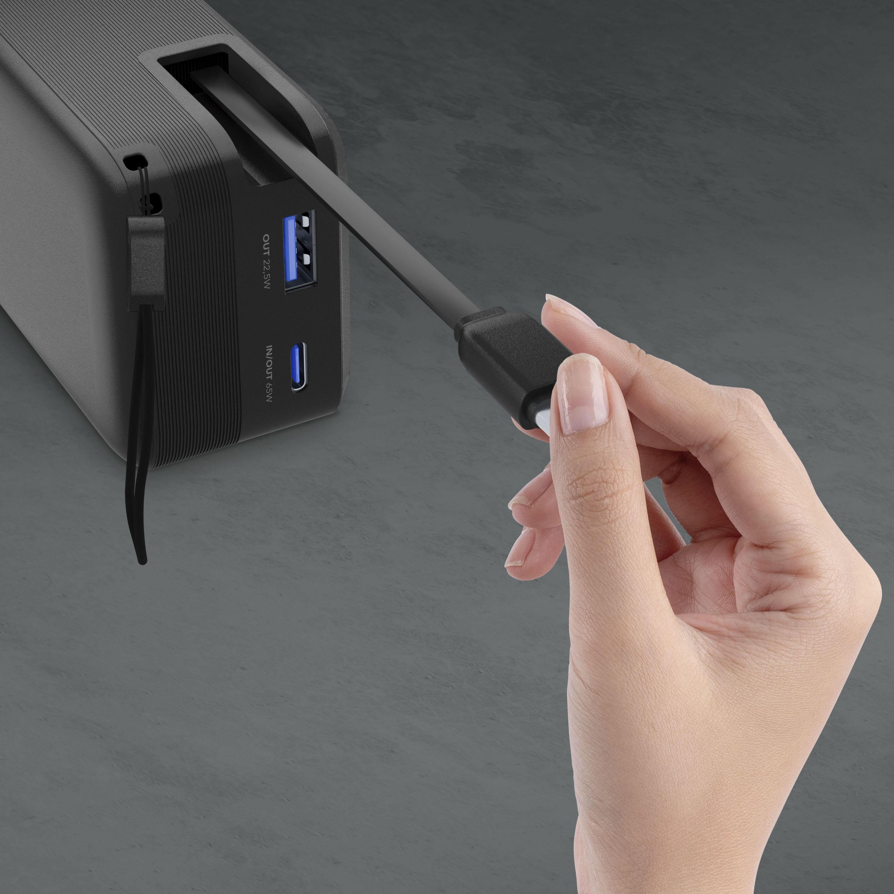 Eine Hand steckt ein schwarzes Kabel in einen schwarzen Powerbank-Anschluss.