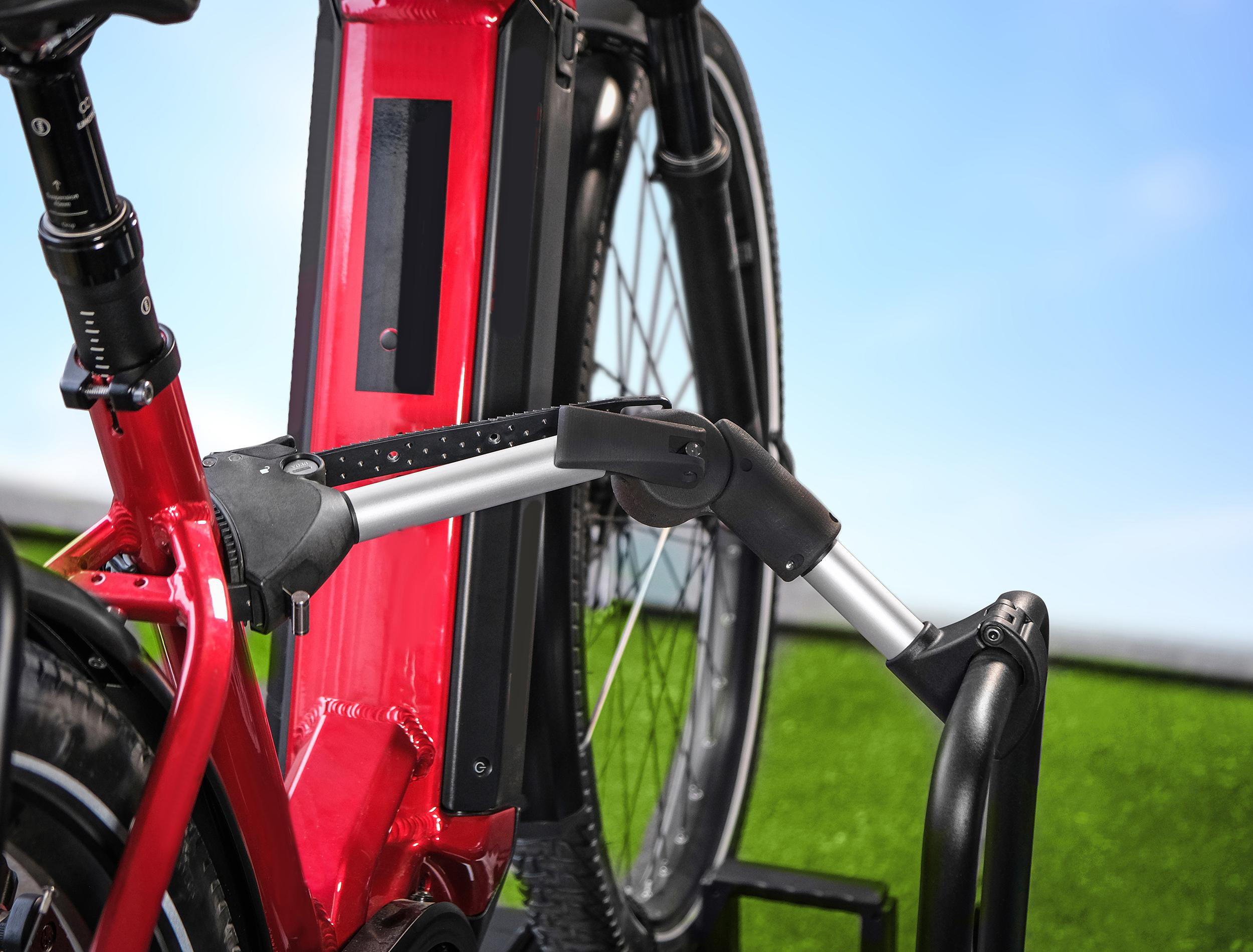 Ein rotes E-Bike mit schwarzem Akku und silbernen Details vor blauem Himmel.