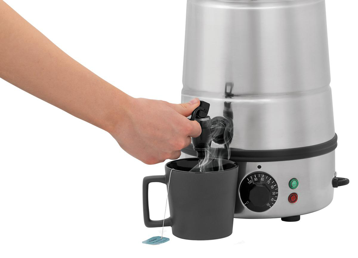 Eine Hand betätigt einen Zapfhahn, heiße Flüssigkeit fließt in eine Tasse mit Teebeutel.