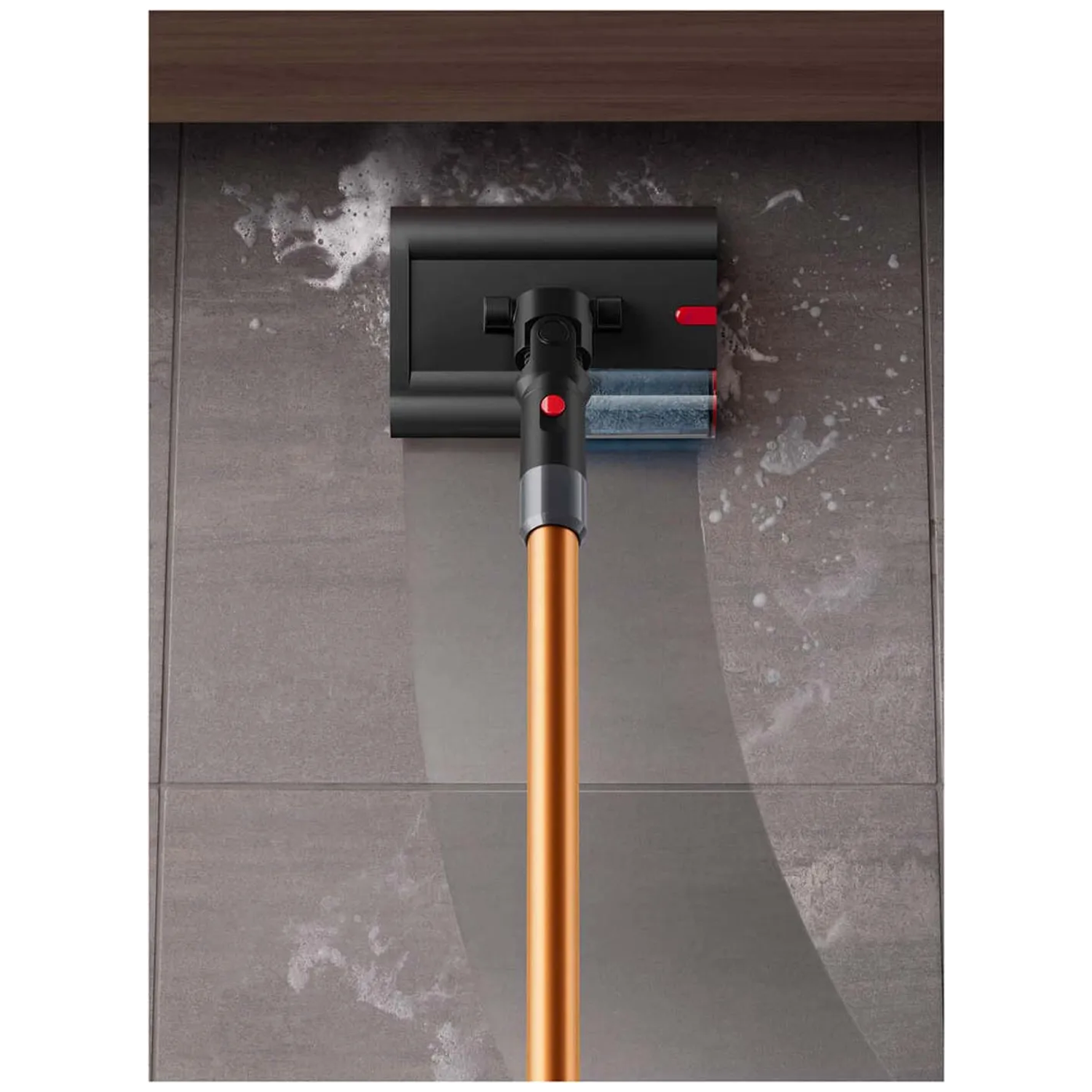 A vacuum cleaner attachment cleans a gray tiled wall with foam.