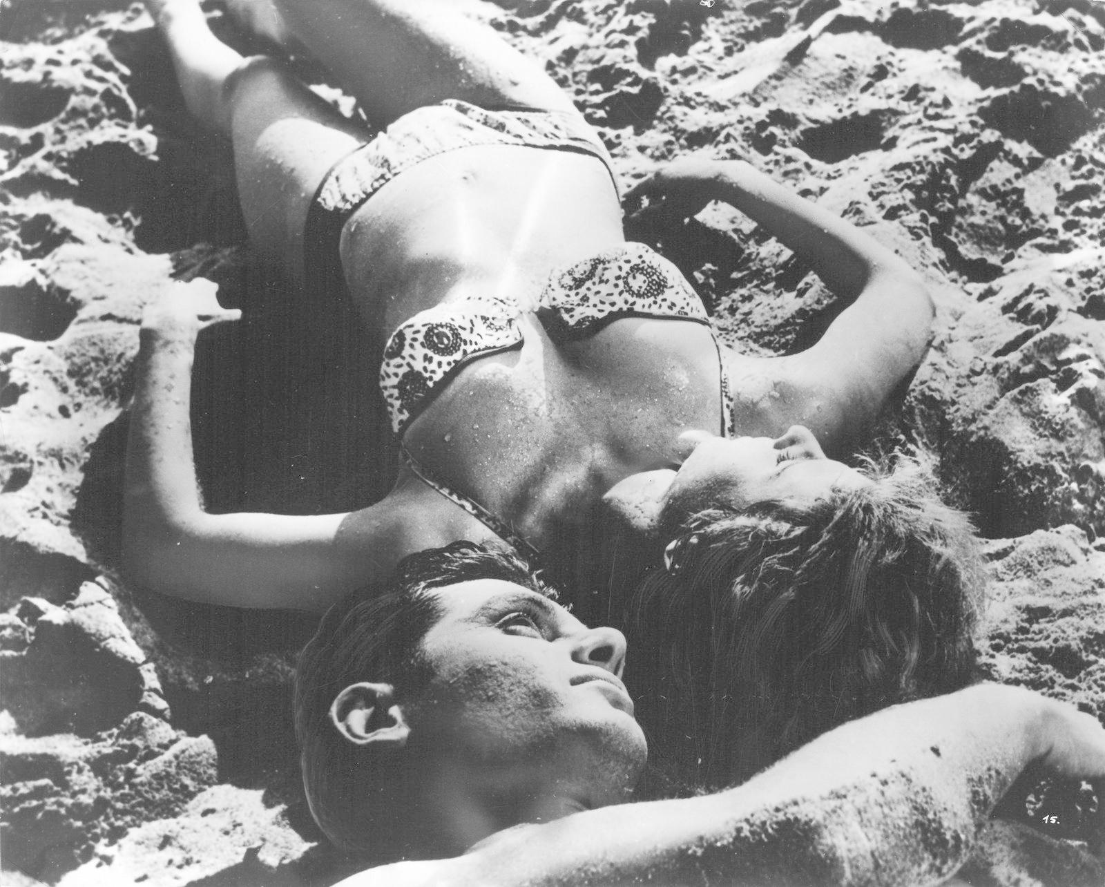 Ein Mann und eine Frau liegen im Sand, beide tragen Badebekleidung.