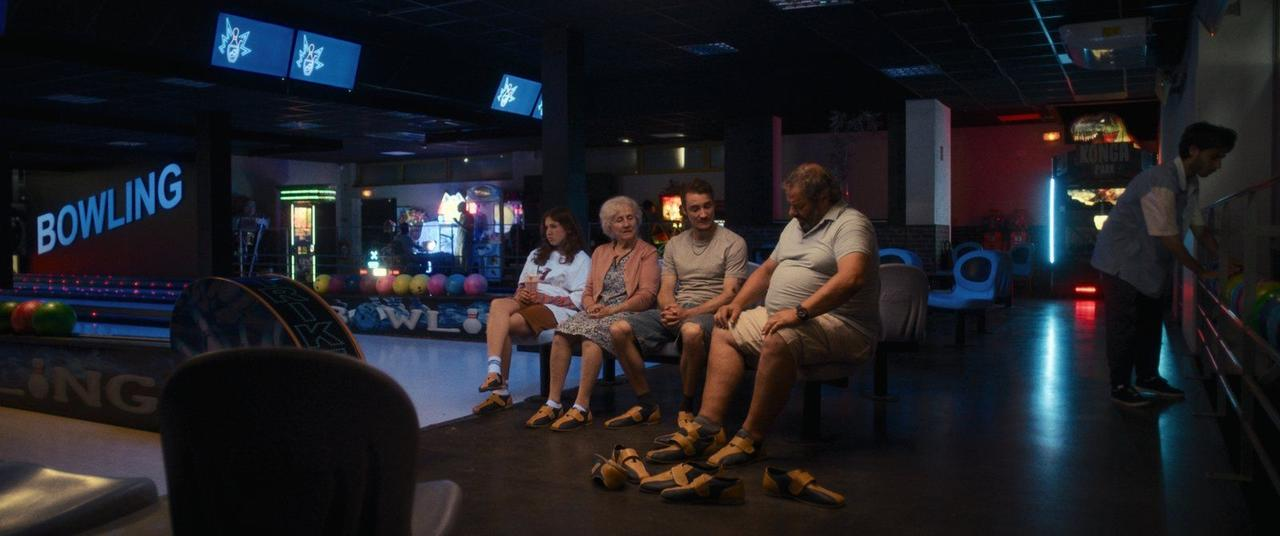 Menschen sitzen in einer Bowlingbahn, die auf das Spiel wartet. Bunte Kugeln sind sichtbar.