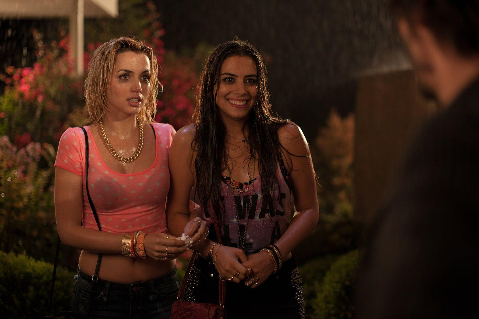 Zwei nasse Frauen stehen im Regen. Eine trägt ein pinkes Polka-Dot-Oberteil, die andere ein Tanktop.