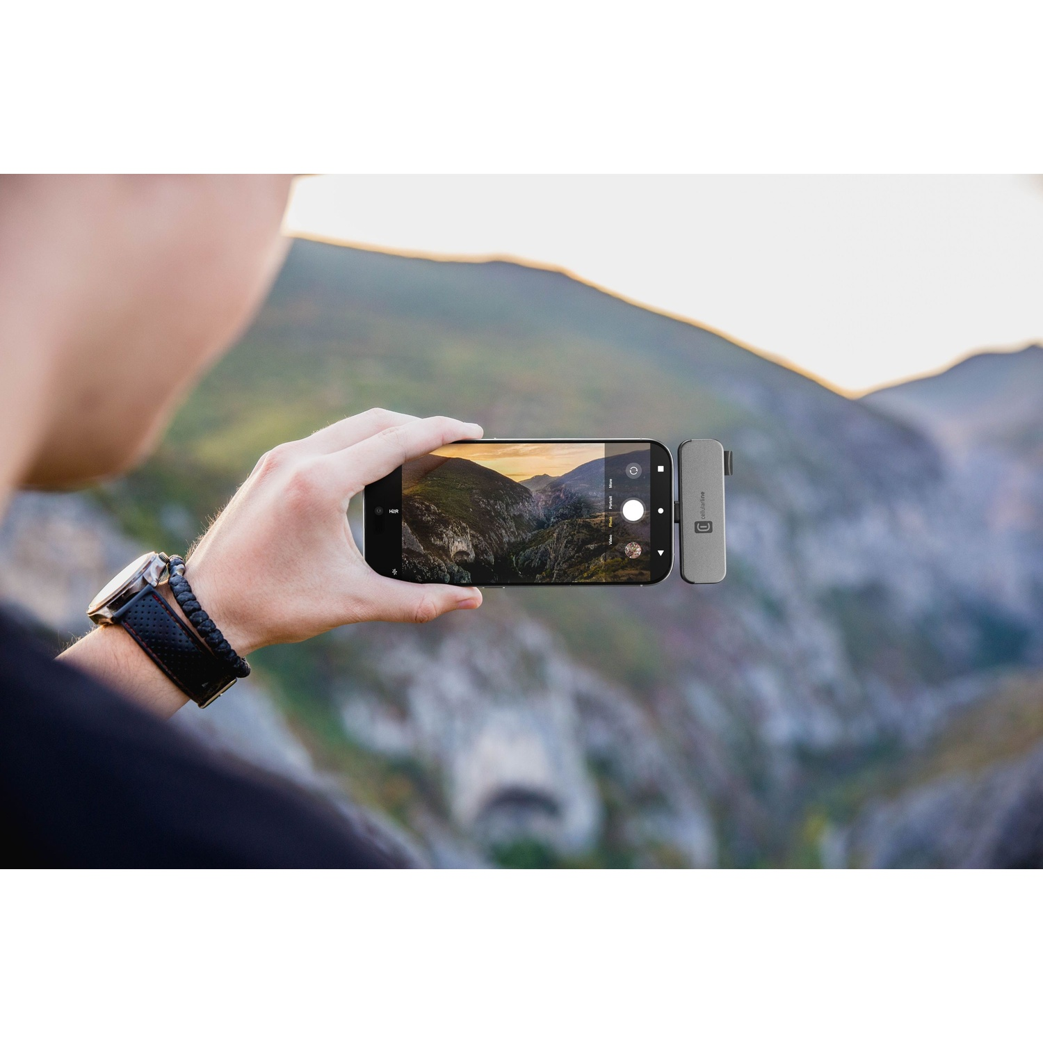 Uomo fotografa paesaggio montano con telefono e microfono esterno.